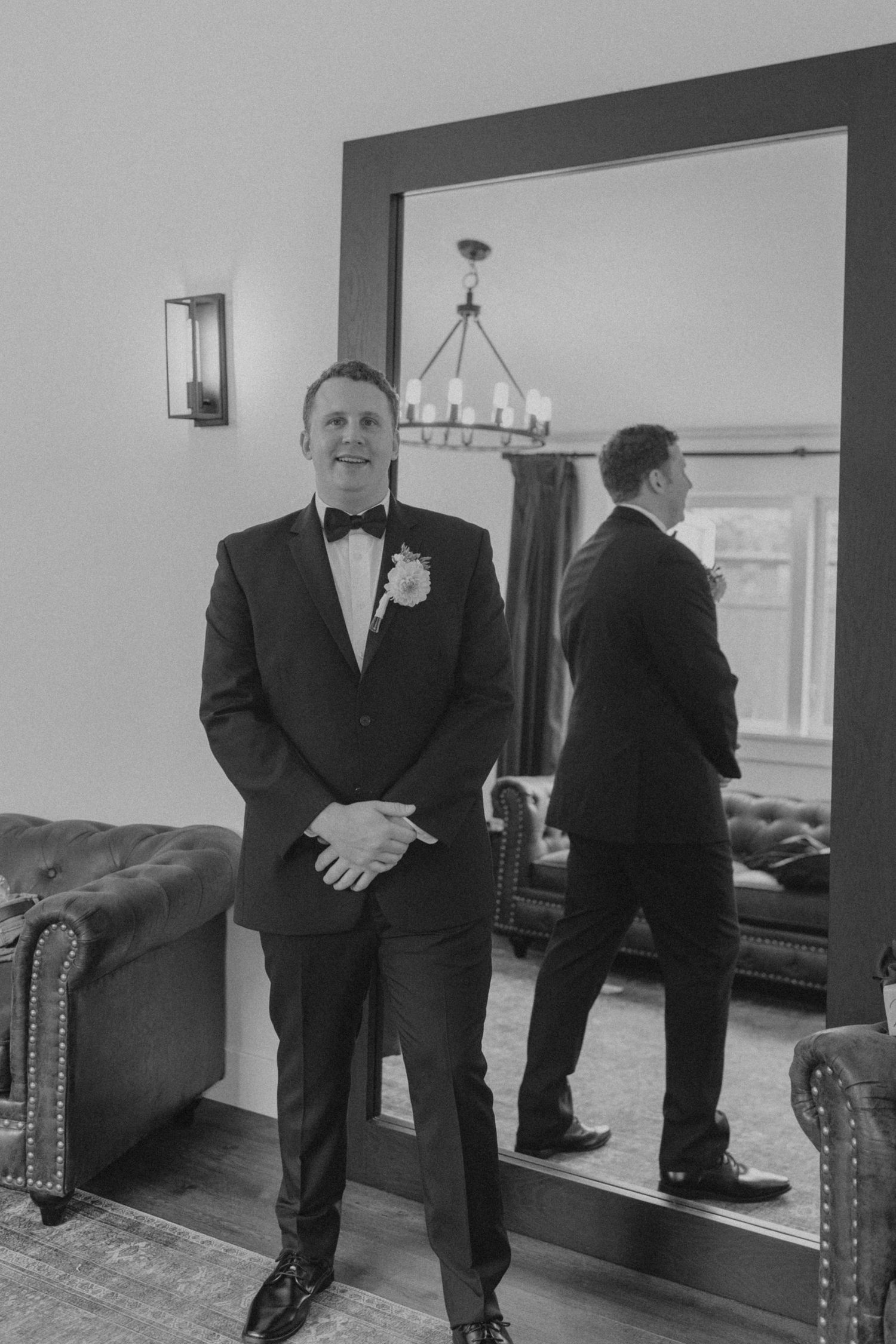 Wedding party members in black tuxedos posing in front of mirrors.