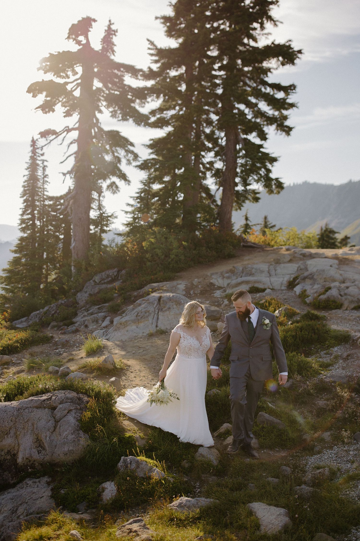Newlyweds walk along rocky mountain trail during golden hour photography session.