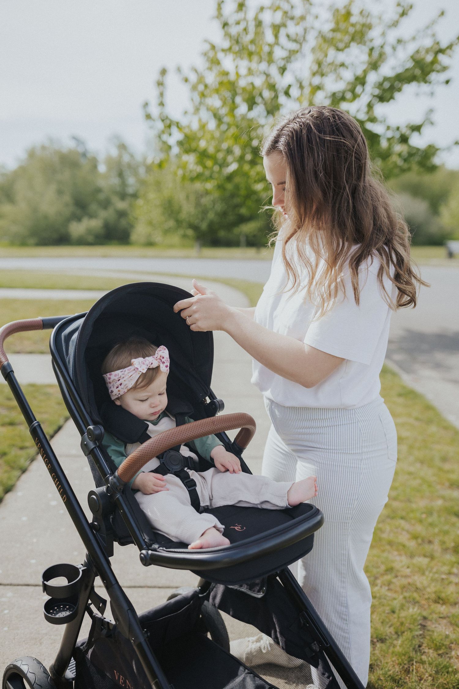 Person in white shirt adjusting black stroller settings on grassy path.