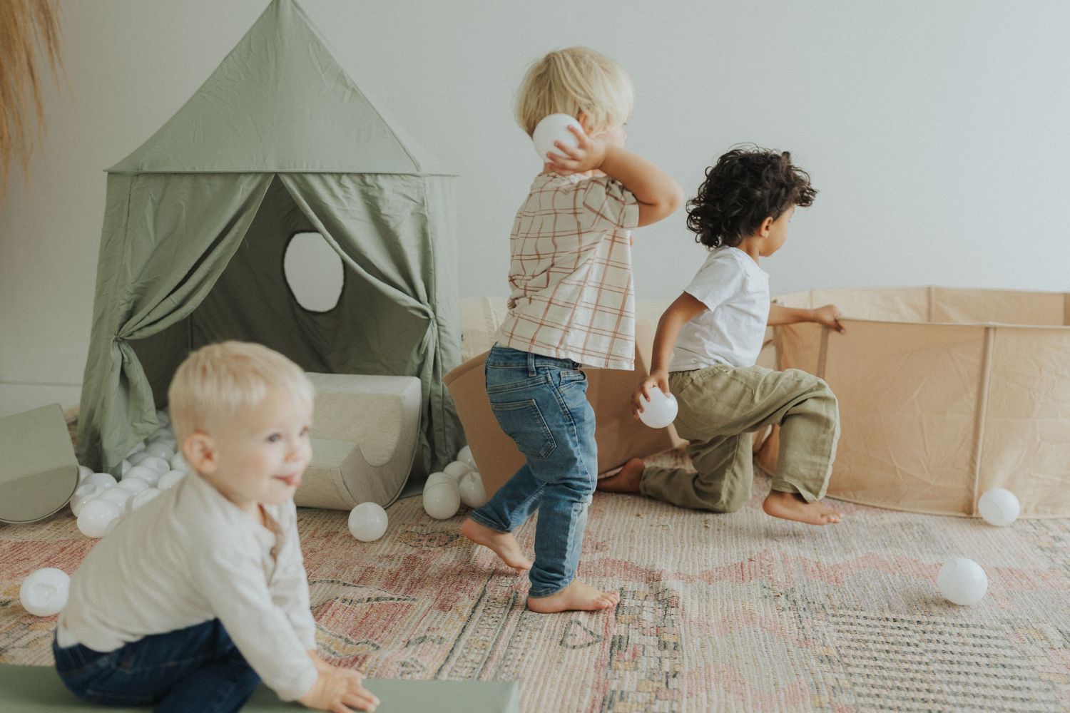 Kids having fun with white balls and a green tent in a bright indoor playspace.