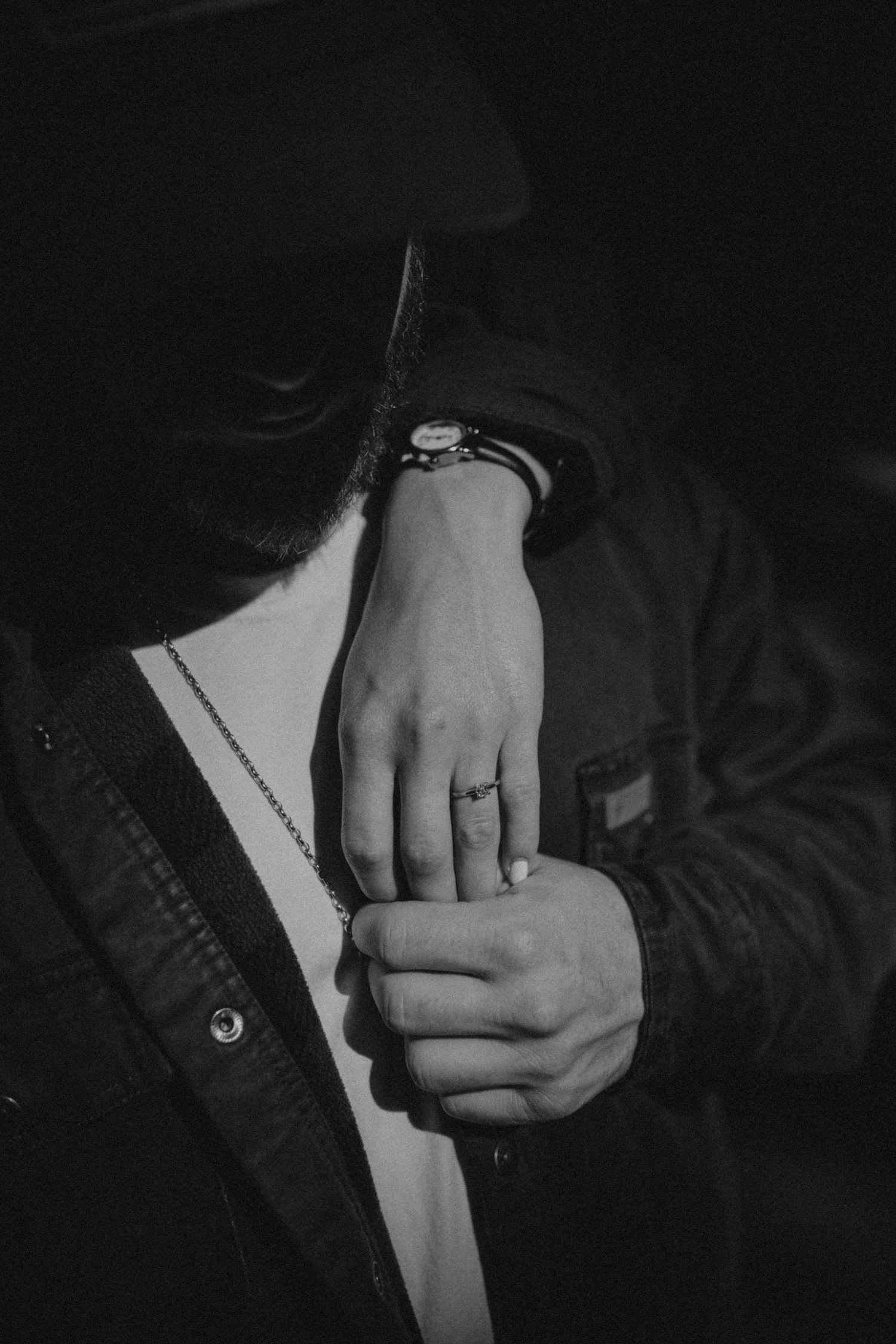 Close-up black and white photo of hands holding each other with an engagement ring visible.