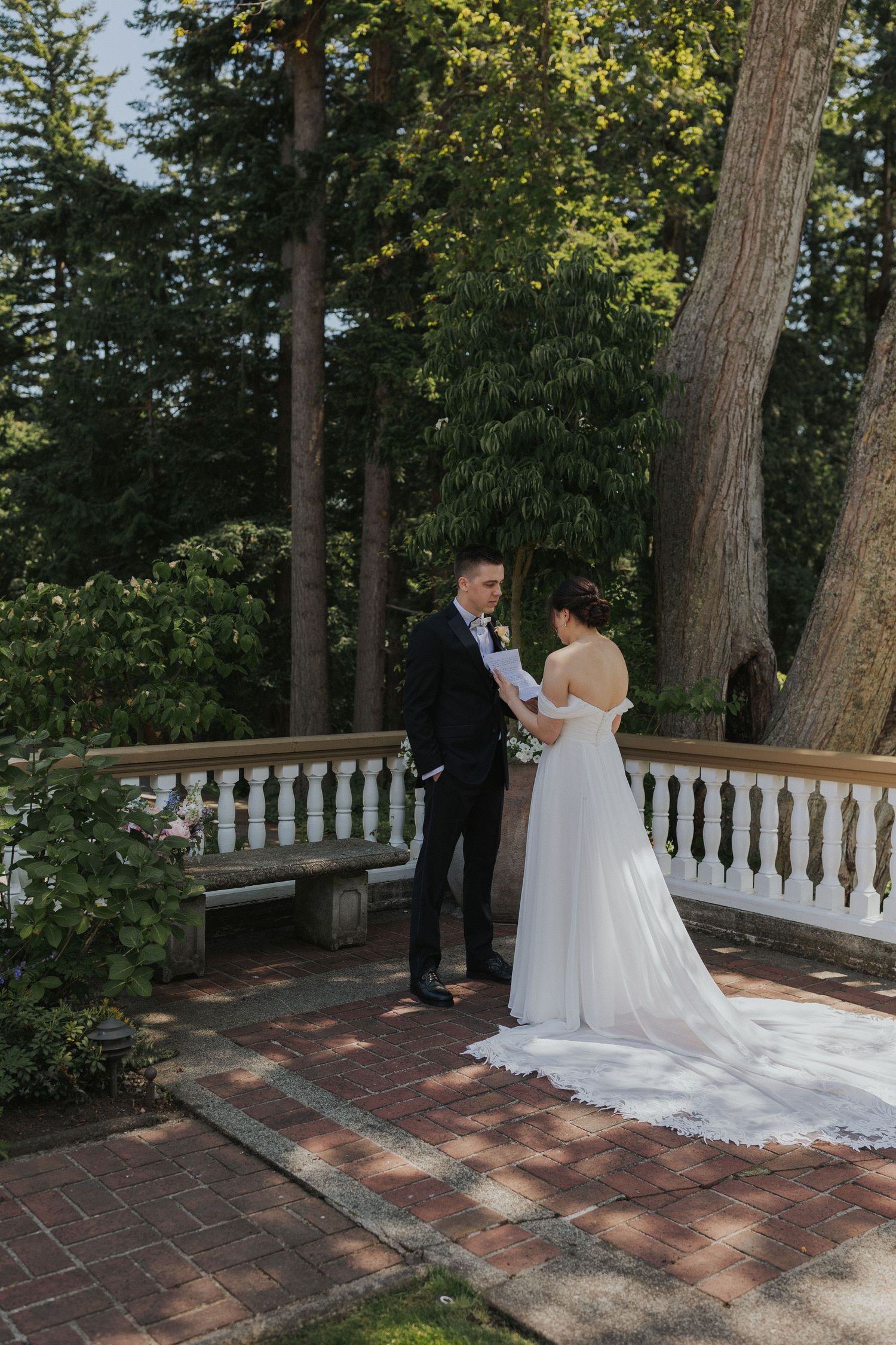 Wedding ceremony taking place on a brick terrace surrounded by tall trees.