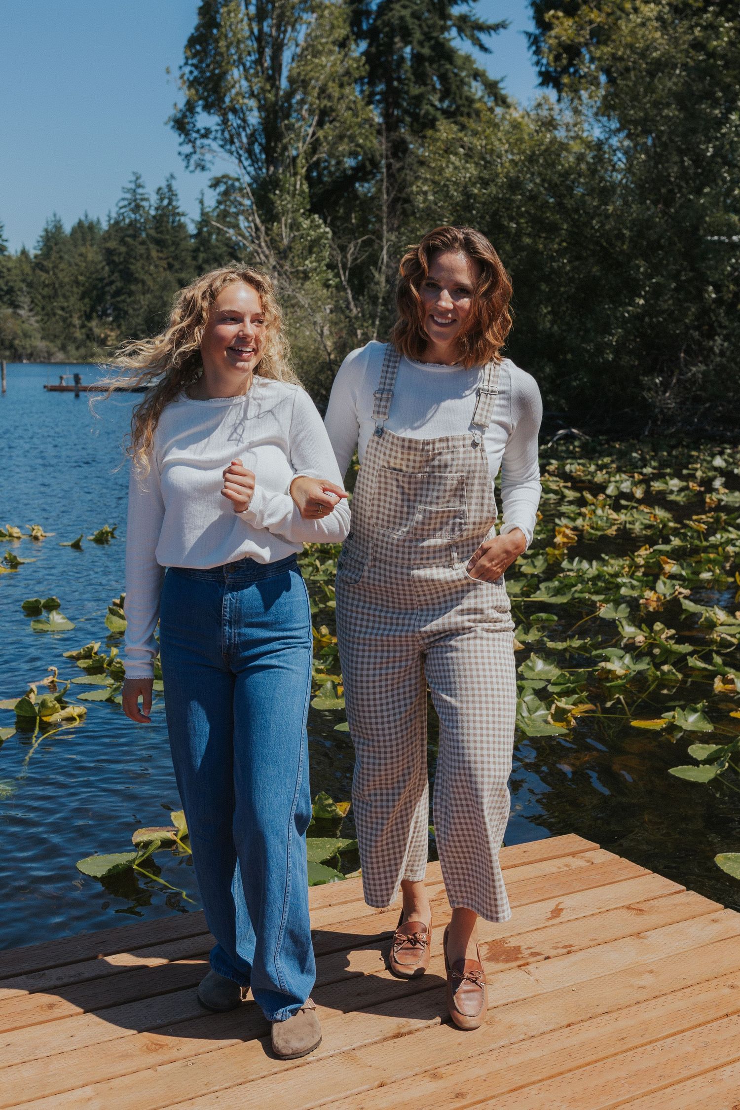 Two people share a moment on a lakeside dock with lily pads visible in the water.