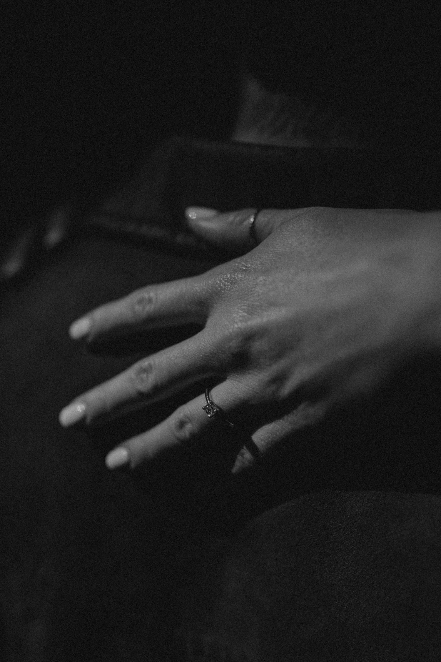 Black and white artistic shot of a hand with ring in moody lighting.