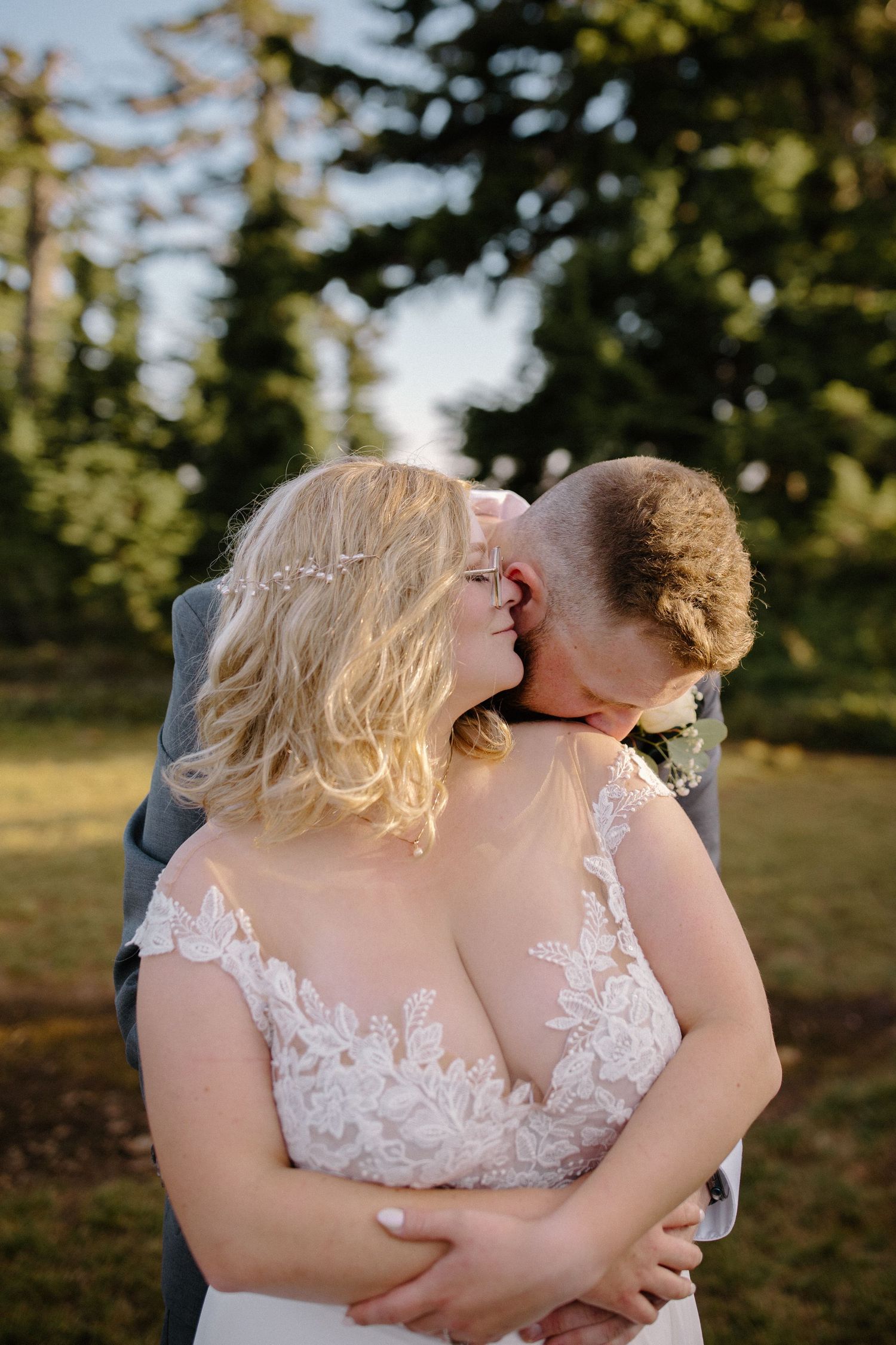 A tender embrace captured in warm sunlight with evergreen trees in the background.