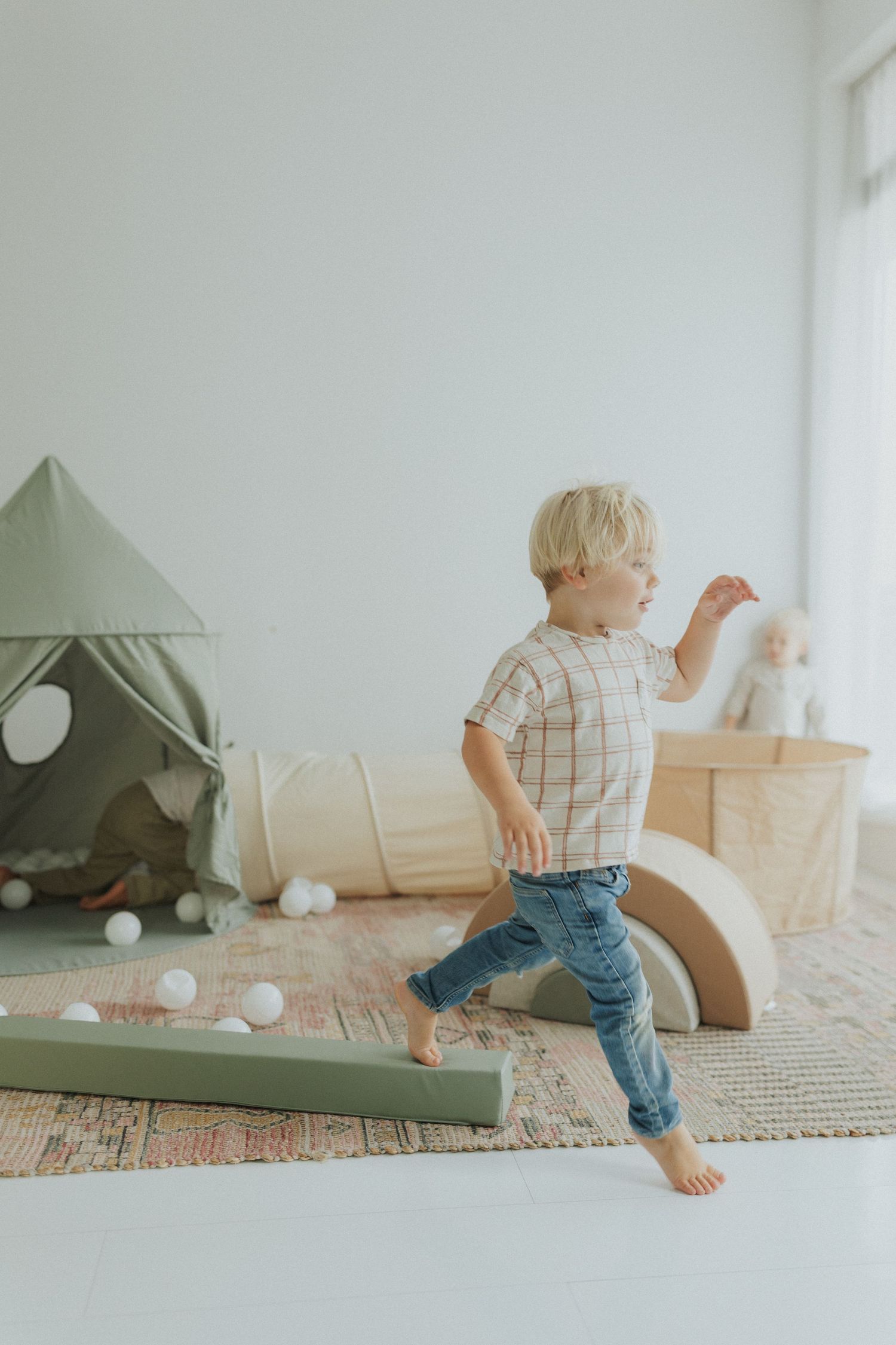 Children playing with white foam balls near a sage green tent in a minimalist room.