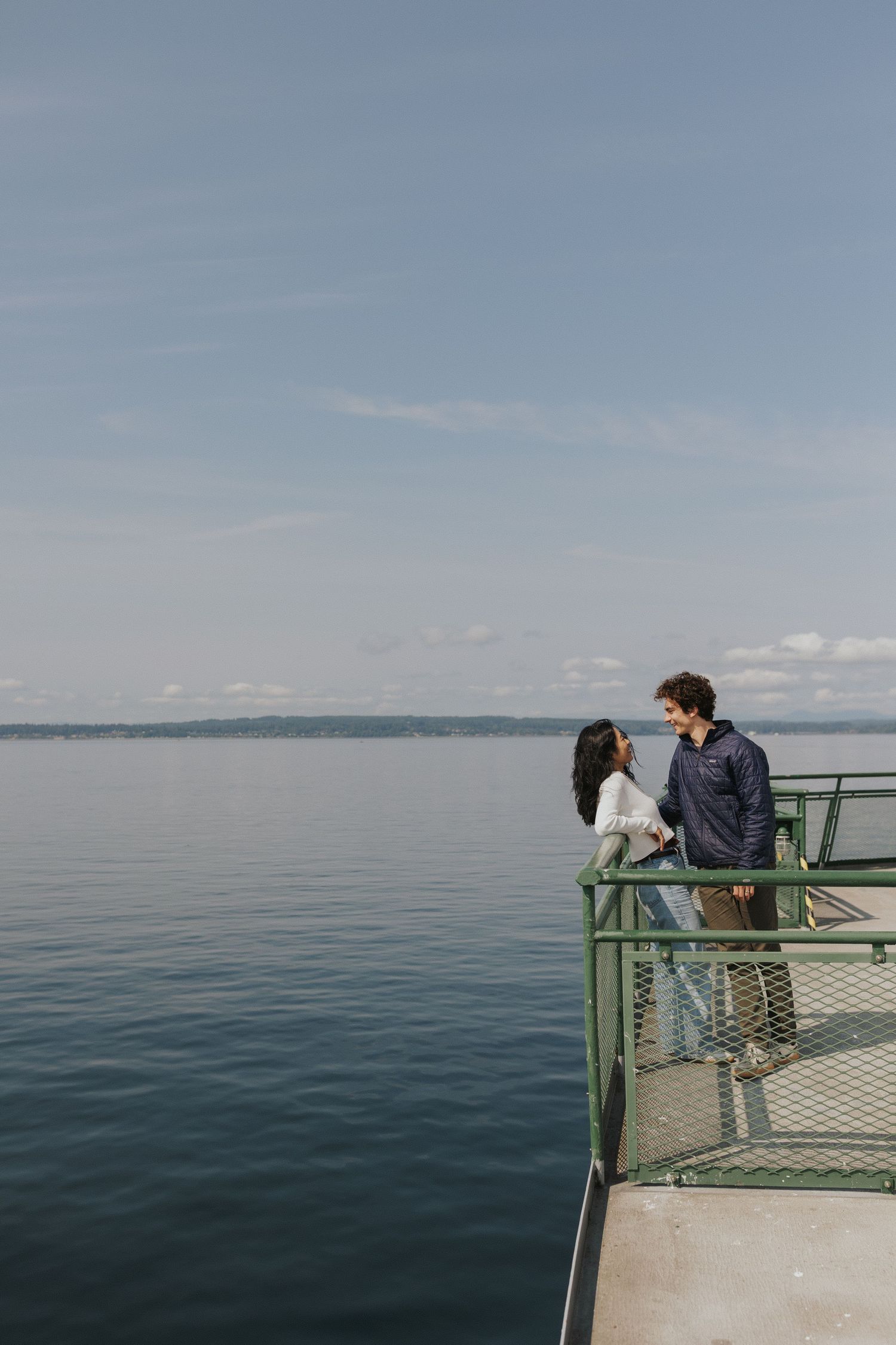 Two people stand on a green-railed observation deck overlooking a vast calm ocean.