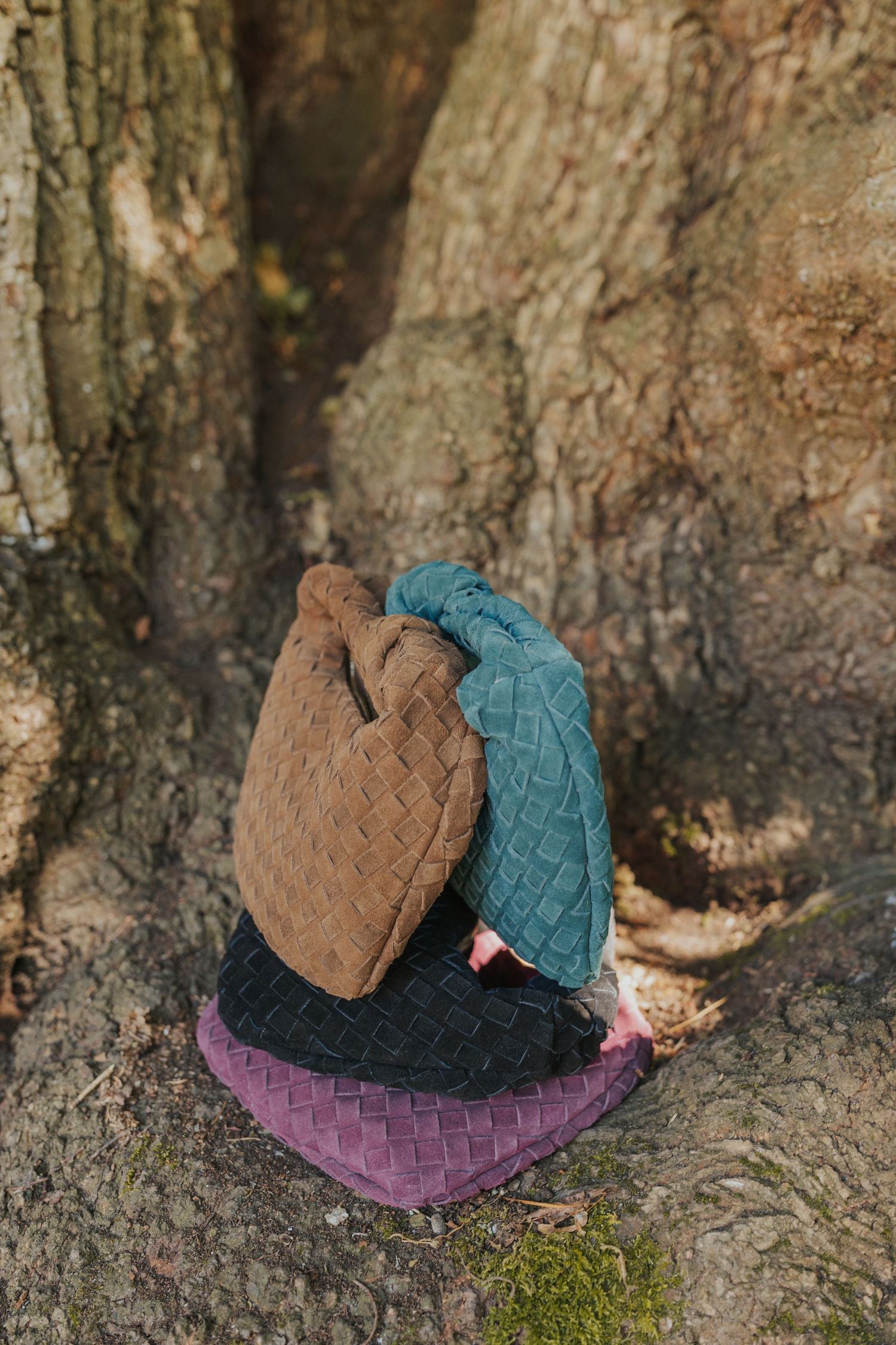 Colorful woven baskets arranged against mossy tree bark in teal, brown, and purple hues.