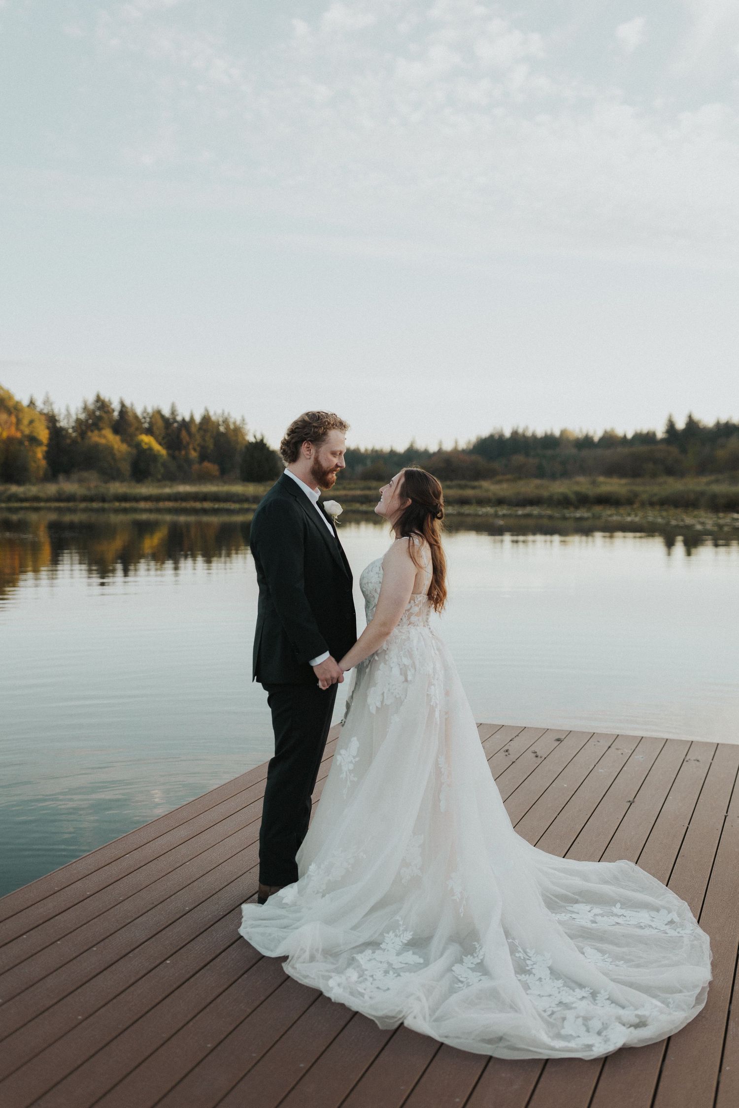 Elegant couple on waterfront deck with fall foliage and calm water reflections.