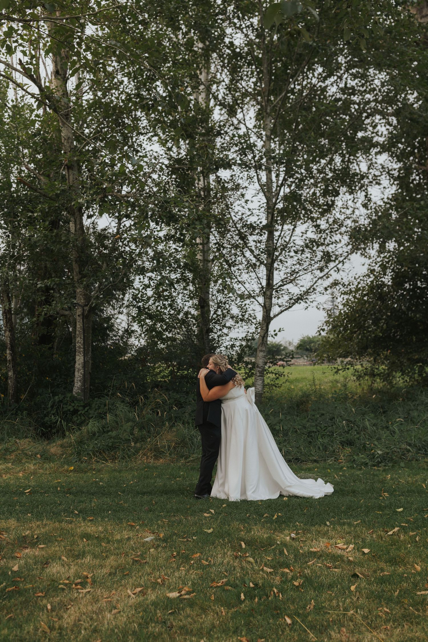 A romantic wedding moment captured in a natural outdoor setting with trees and grass.