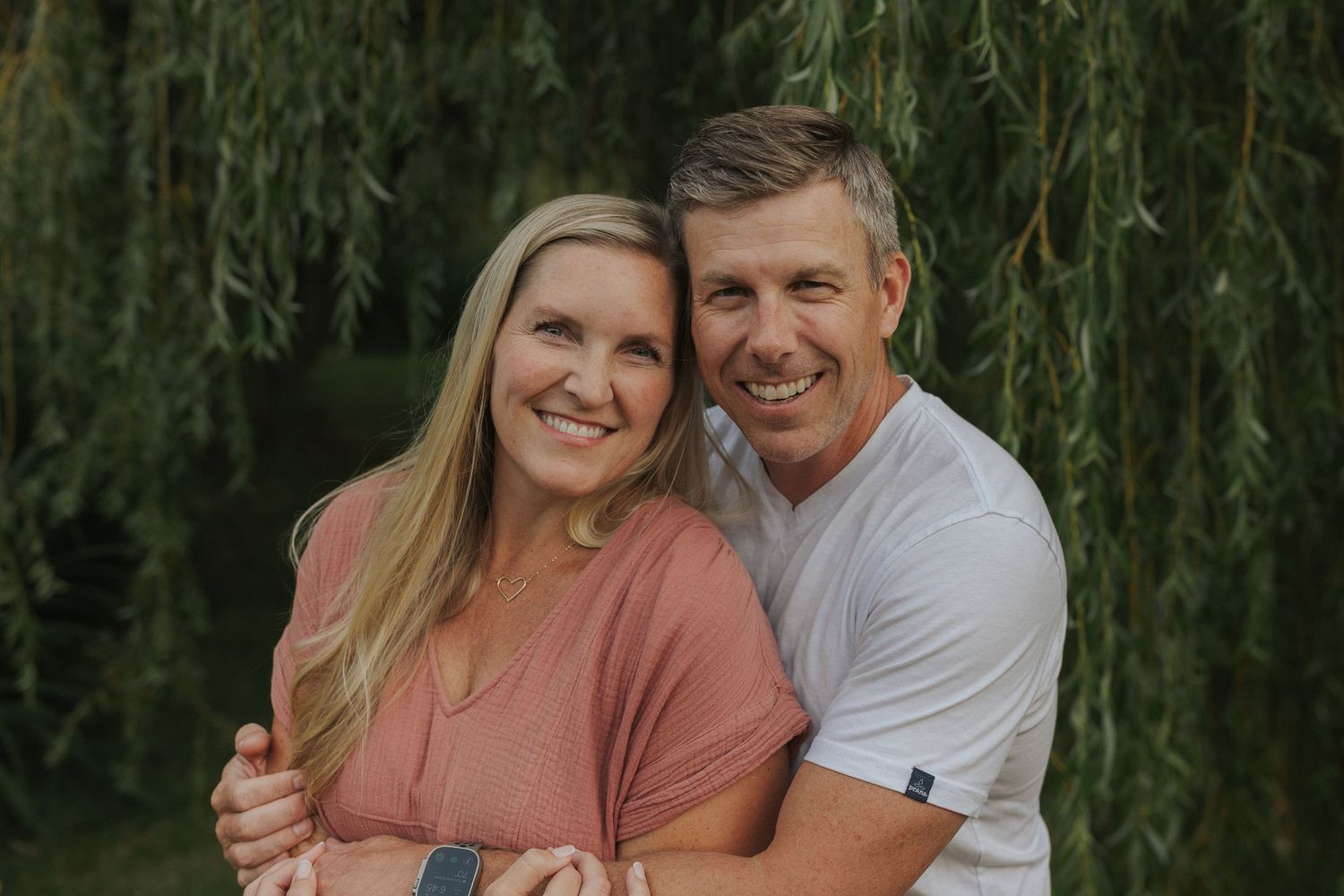 Couples posing together under drooping willow branches in summer setting.