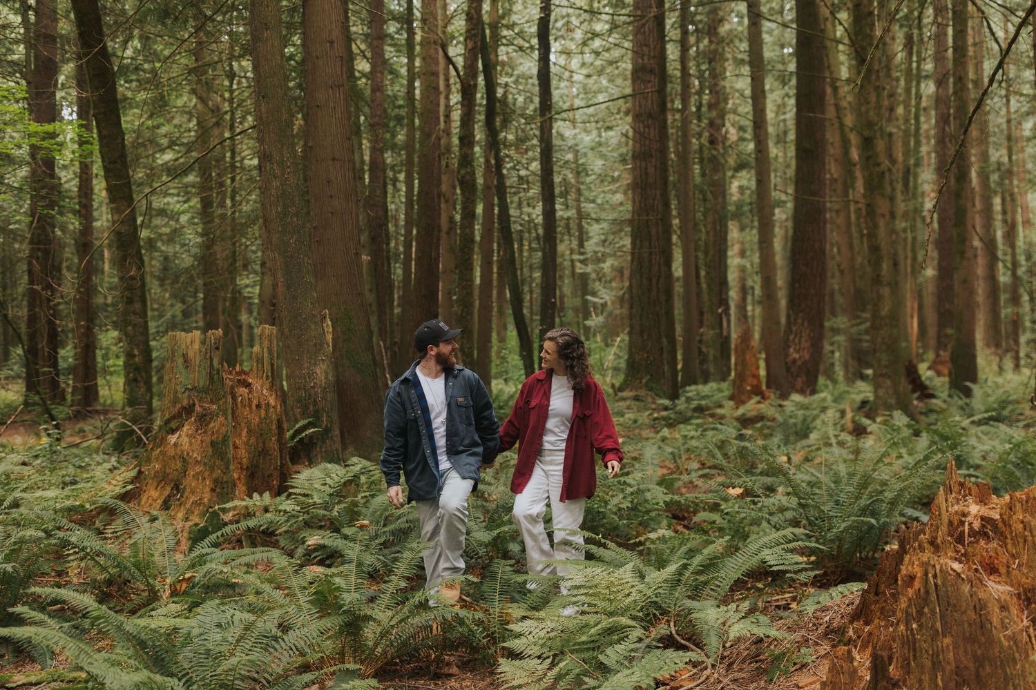 Two people share a tender moment on a forest path surrounded by evergreen trees.