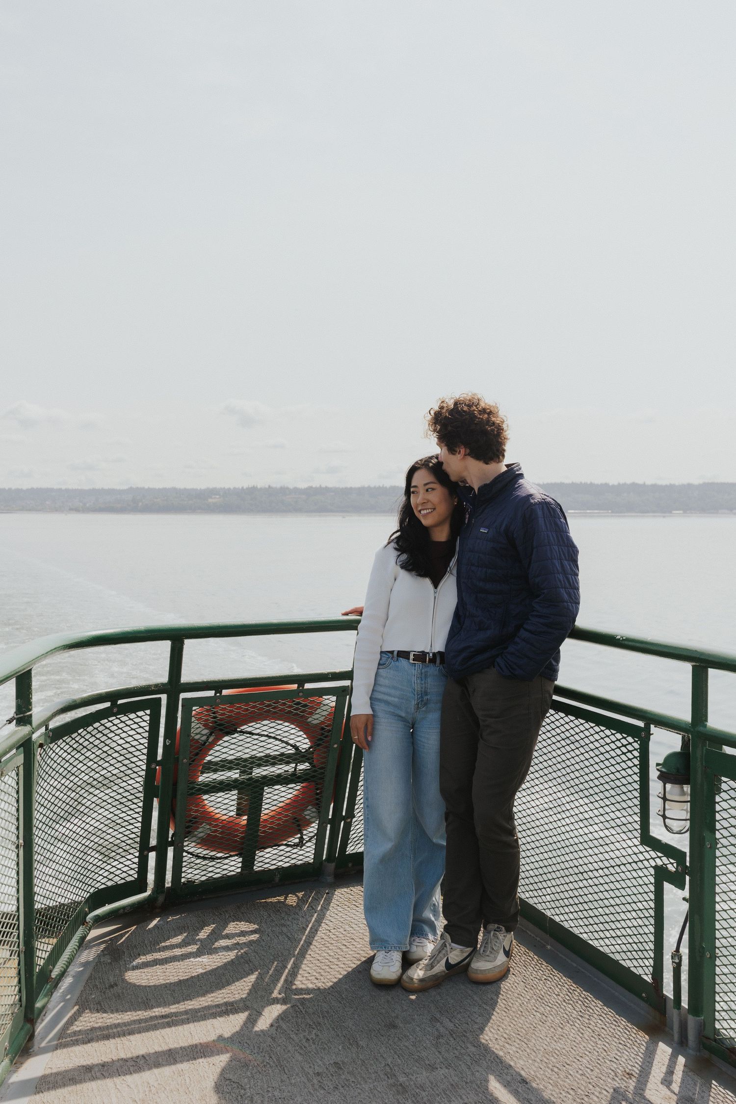 Couple sharing intimate moment by green ferry railings overlooking water.
