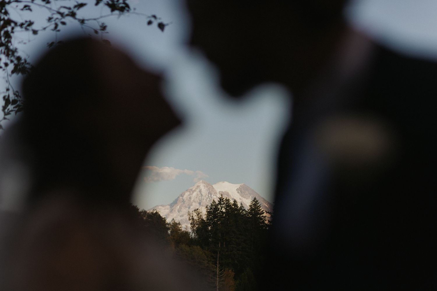 Scenic mountain vista framed between blurred foreground silhouettes at sunset.