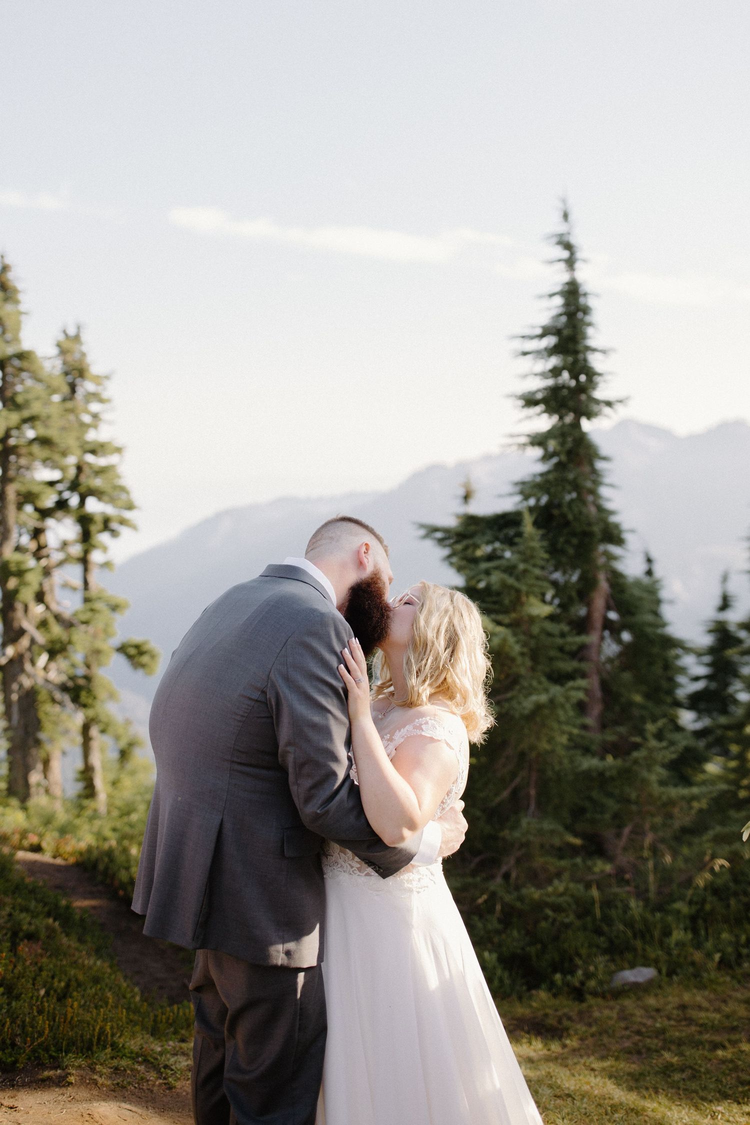 A couple shares their first kiss as newlyweds with mountains in the background.