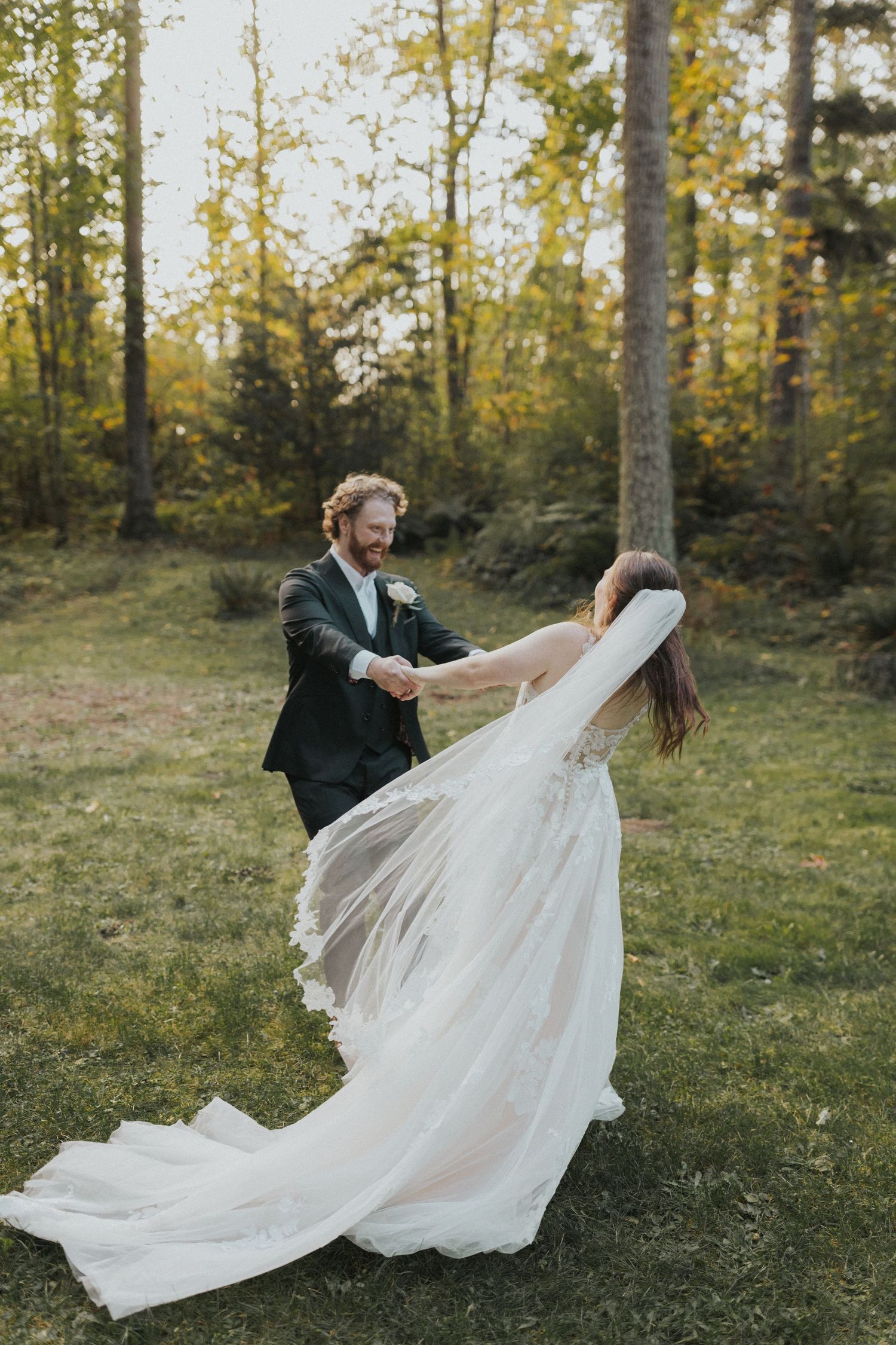 Couple dancing playfully in a forest clearing with bride's dress flowing in the wind.