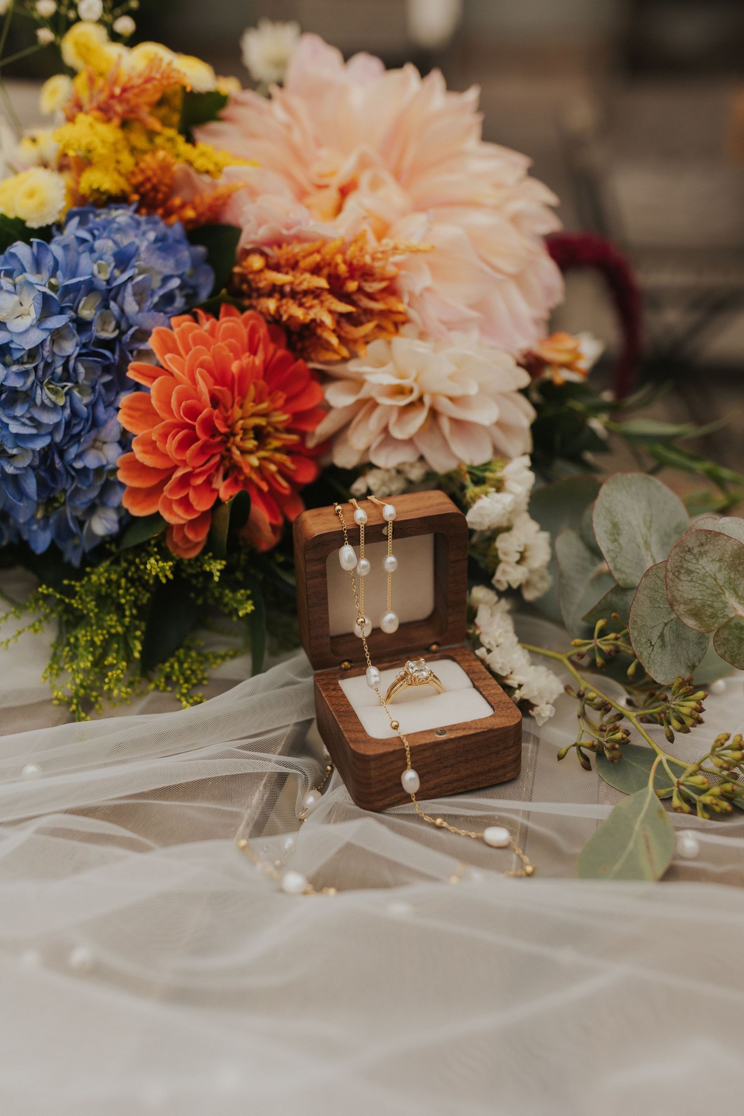 Colorful wedding floral arrangement with dahlias, hydrangeas and jewelry box on white fabric.