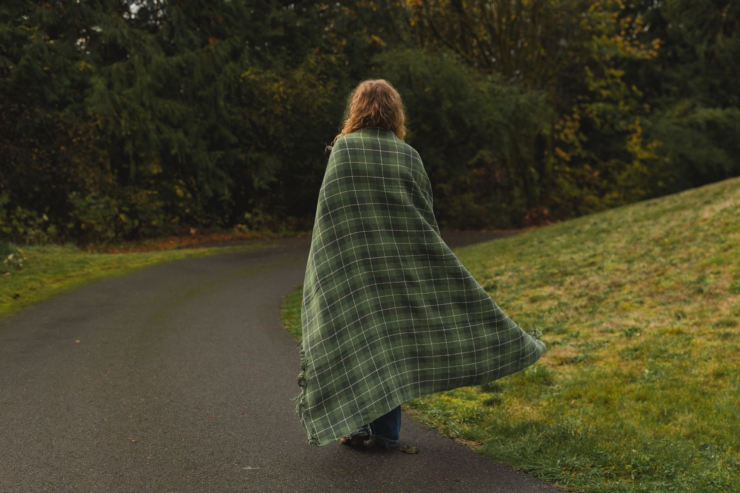 Person wearing a green plaid outfit walking along a curved path during fall season.
