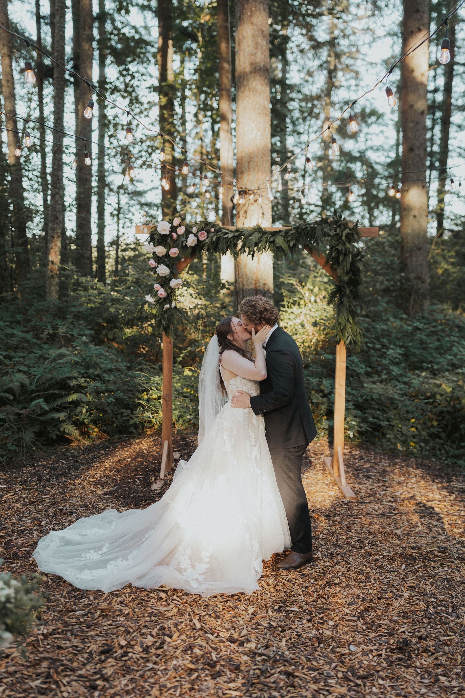 A romantic wedding moment captured in a sunlit forest with fallen autumn leaves.