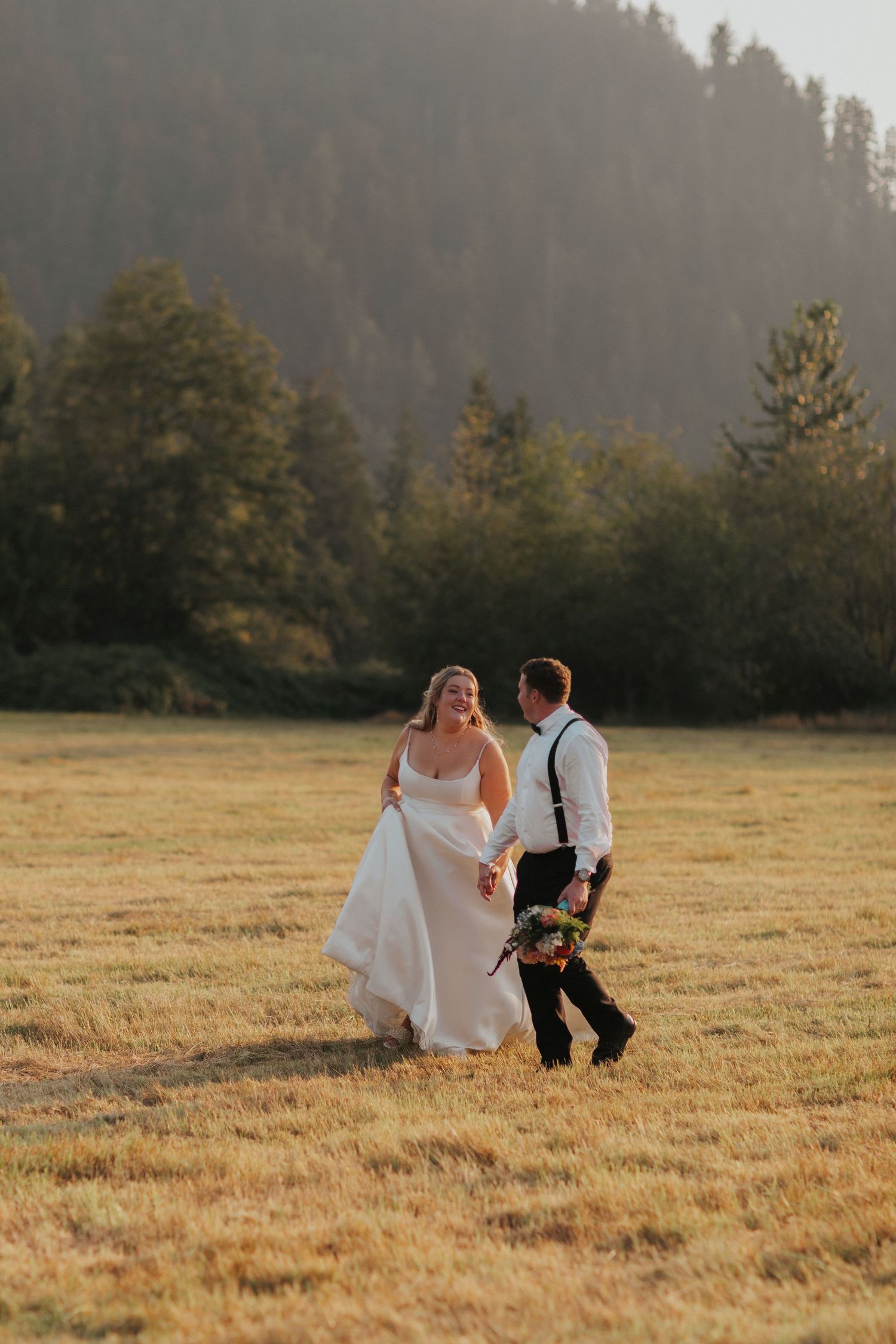 Couple walking with their dog across a scenic field during sunset.