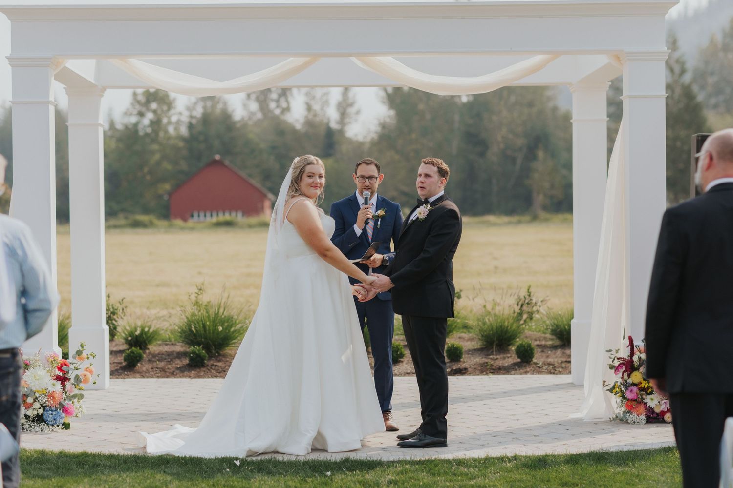 White pergola wedding ceremony space with elegant draping and floral decorations.