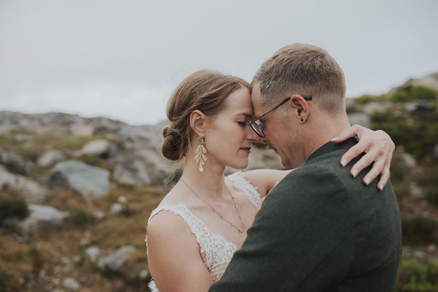 Close-up wedding portrait against mountain landscape with dramatic clouds.