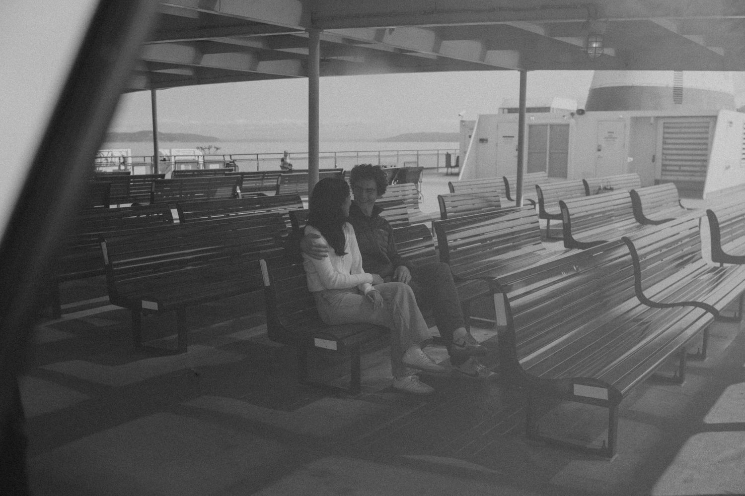 Black and white photo of passengers sitting on benches aboard a ferry boat deck.