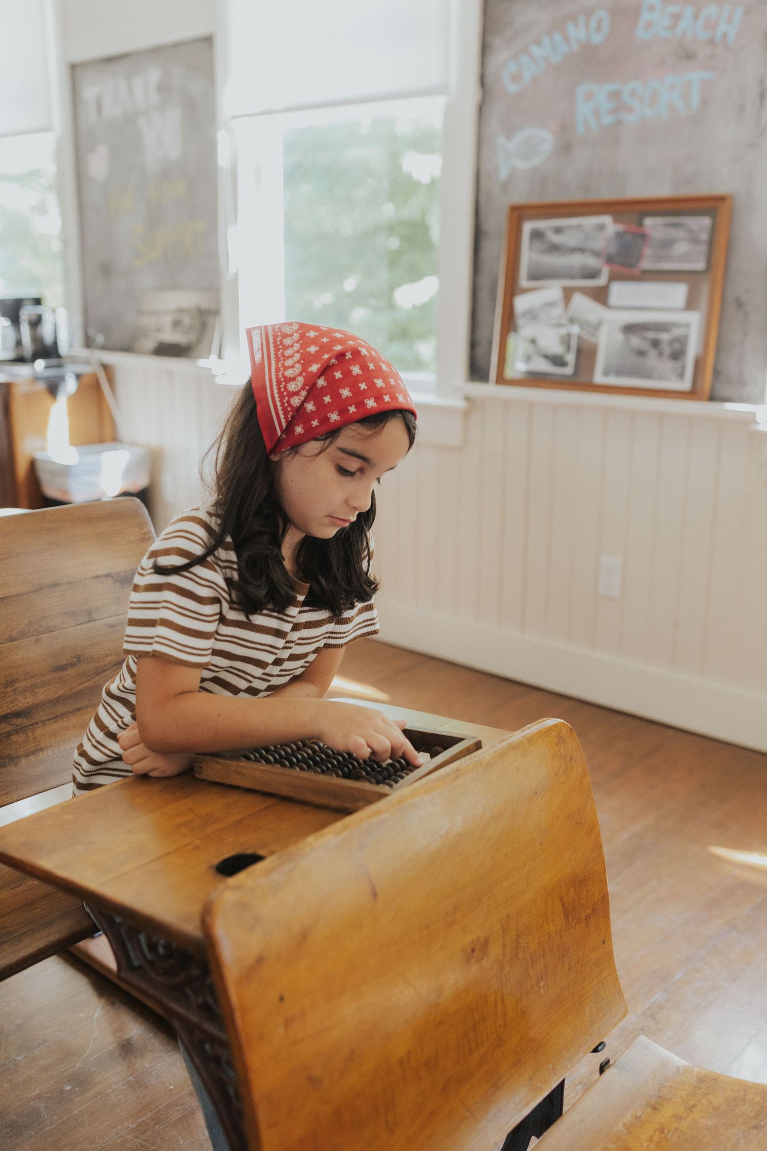 Student in red bandana working at vintage wooden school desk in classroom.