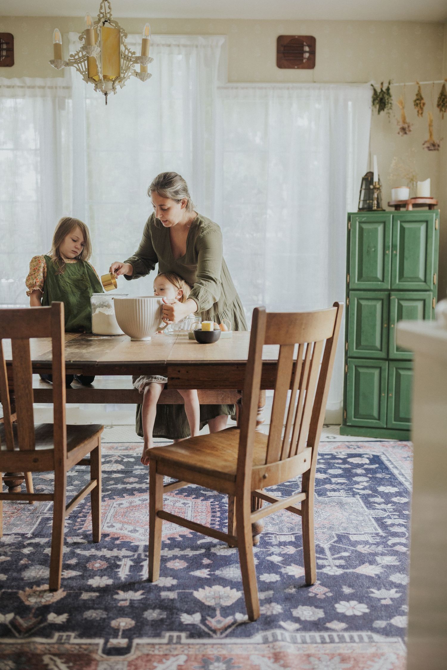 Dining room with wooden table, chairs and vintage green cabinet against white walls.