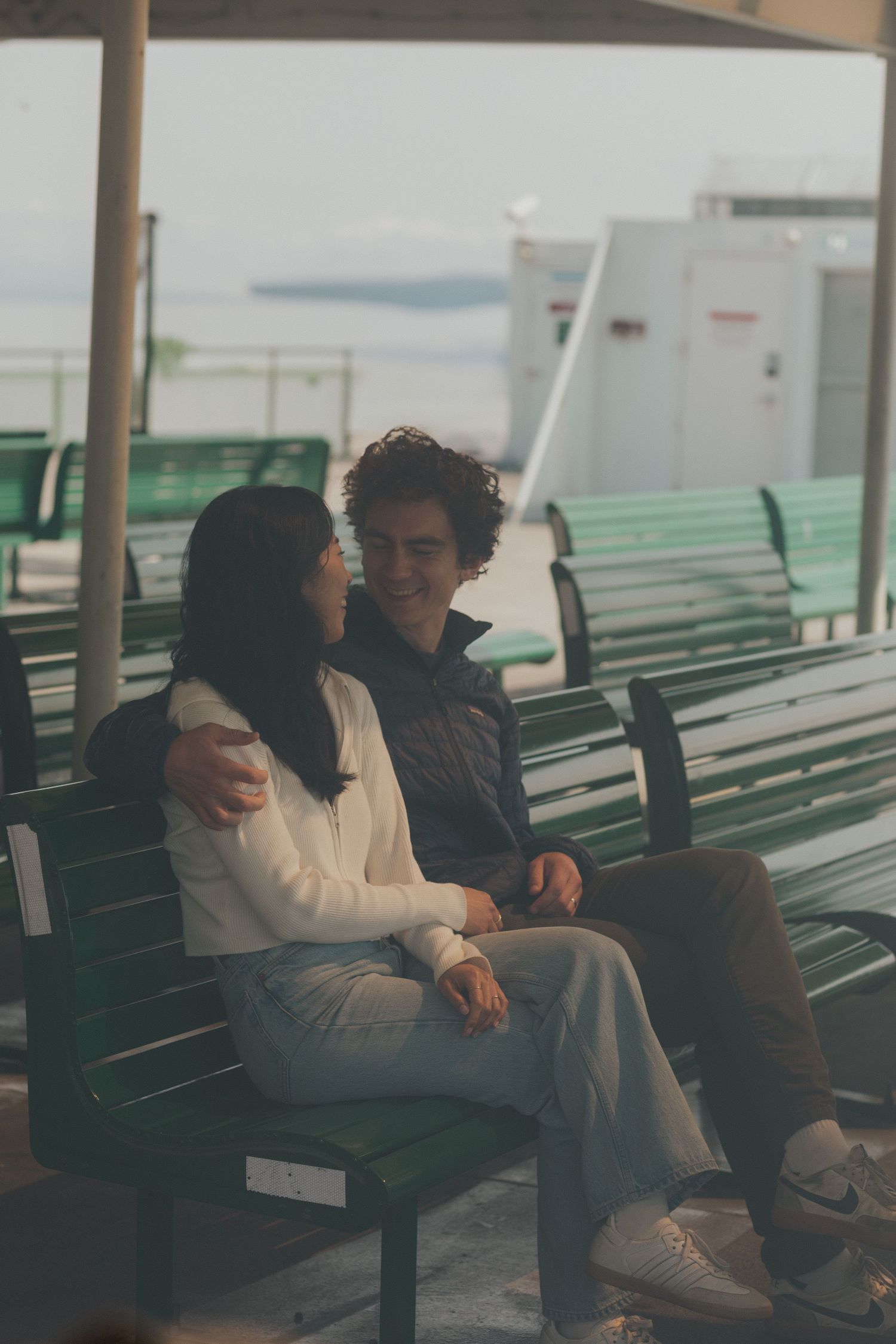 A couple sits intimately together on a bench aboard a ferry boat deck.