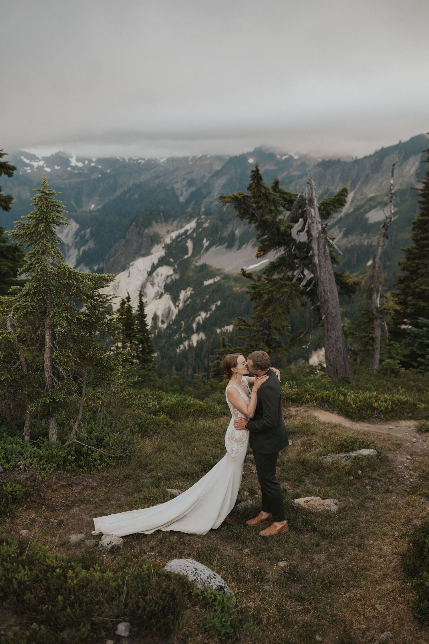 Intimate wedding moment captured on mountain trail with sweeping valley views and evergreen forest.
