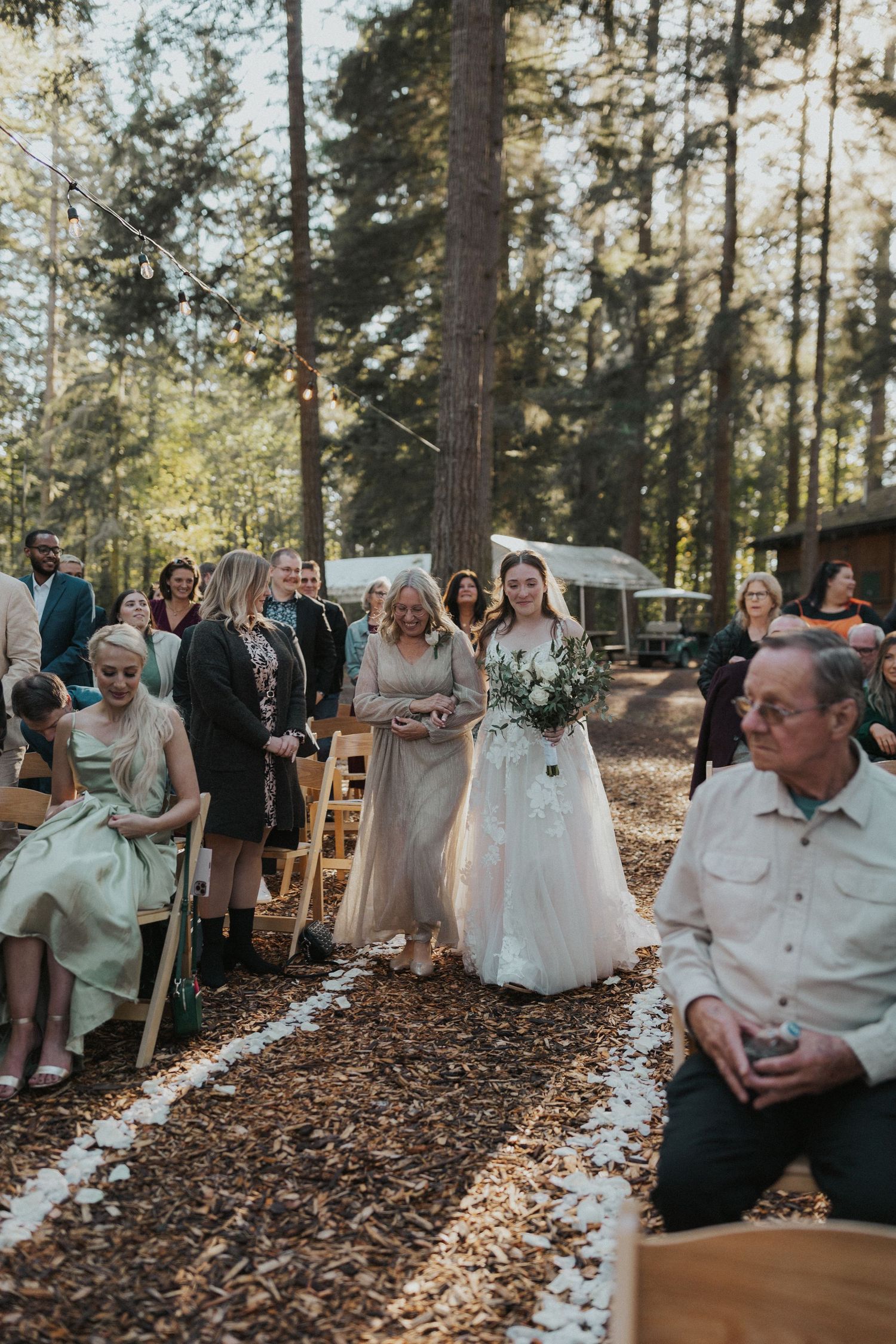 A wedding ceremony in a forest setting with wooden chairs arranged on fallen leaves.