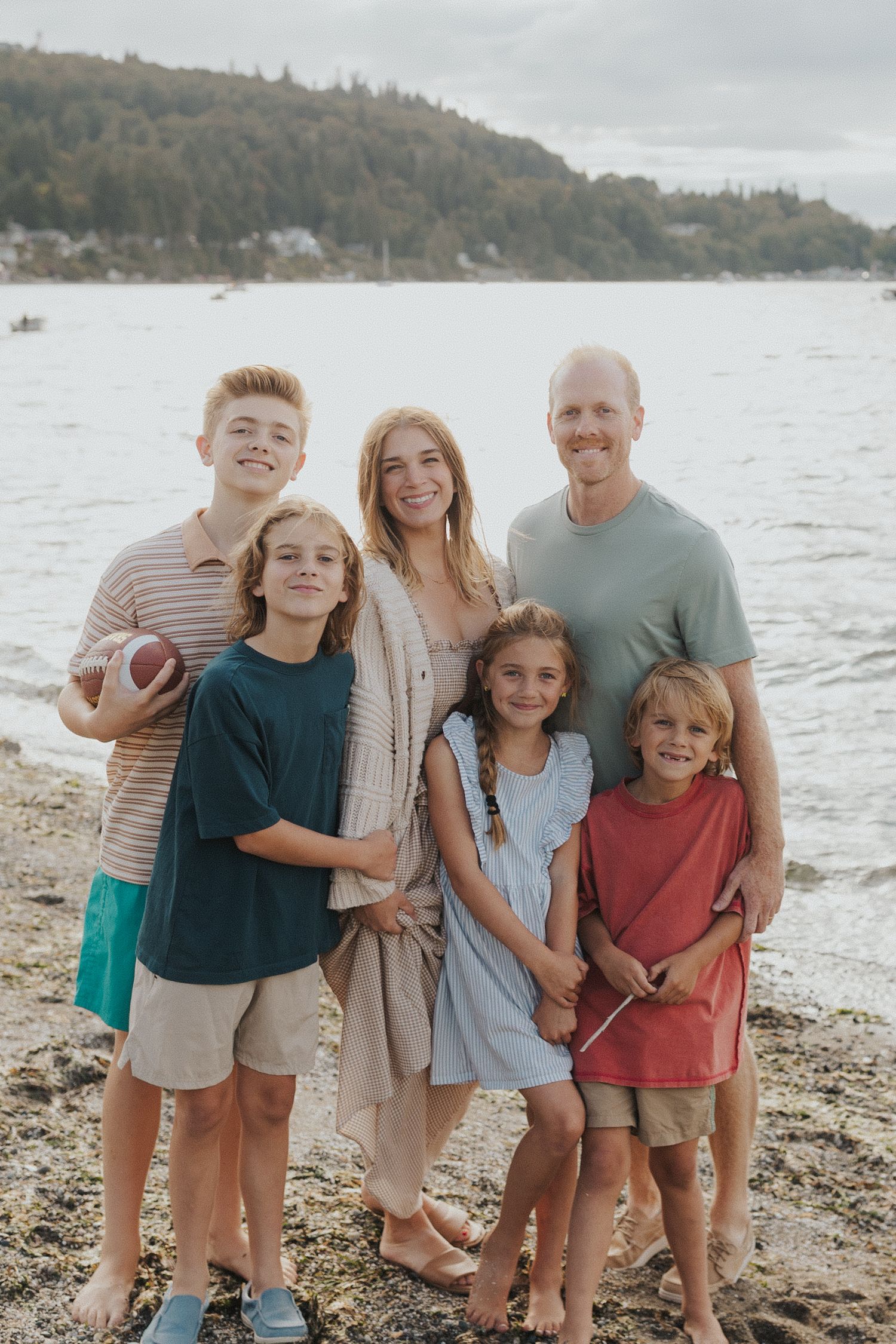 Family group portrait on a pebbly beach with water and mountains in the background.