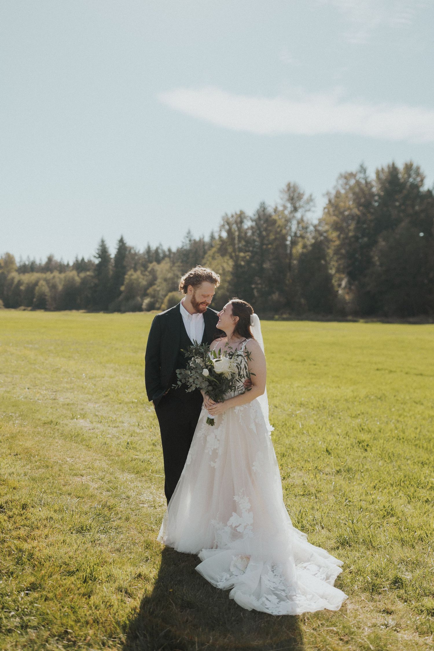 Romantic wedding portraits captured in a green meadow with forest backdrop on a bright autumn day.