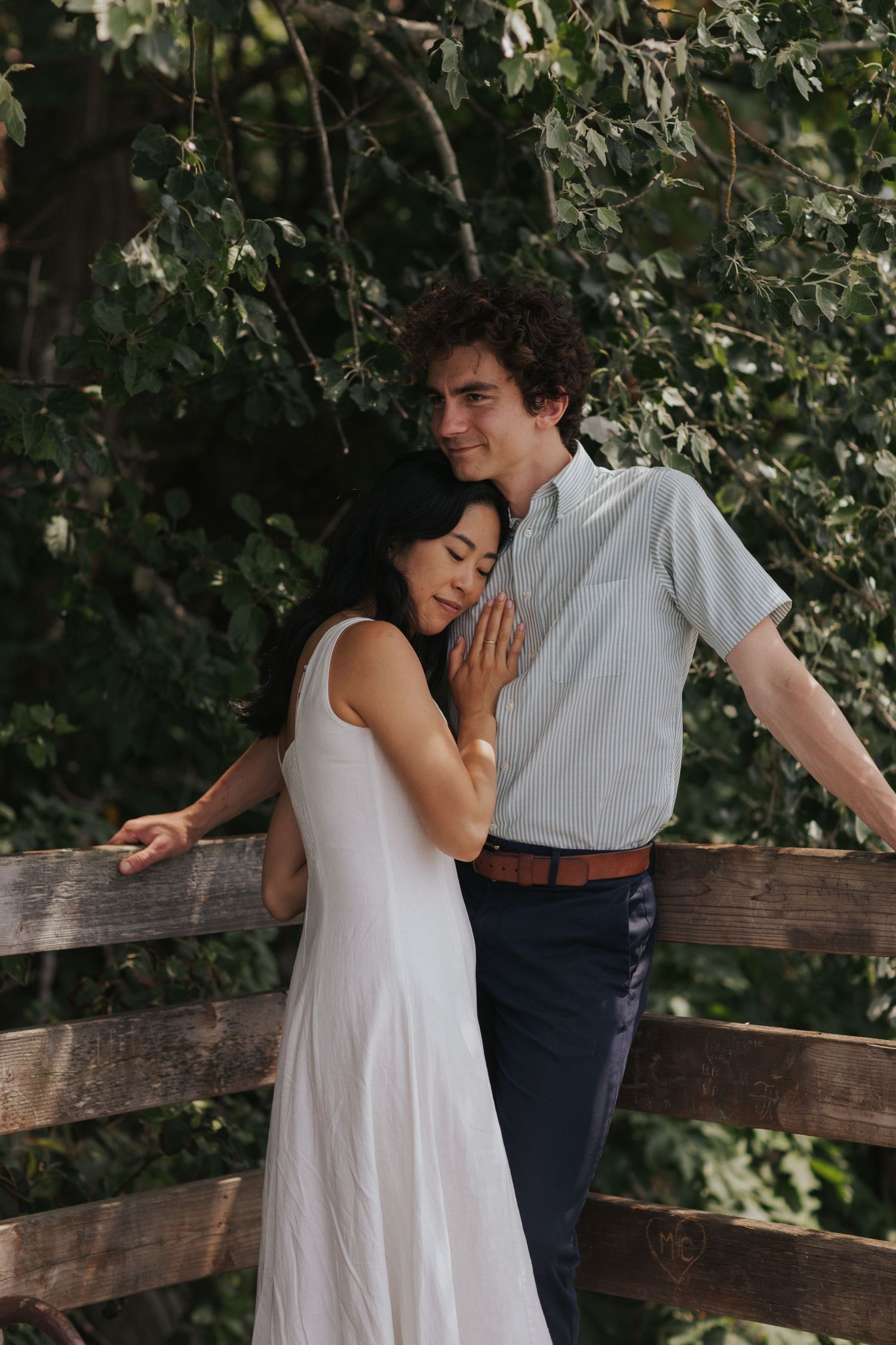 Couple in white dress and navy pants embracing on wooden deck.