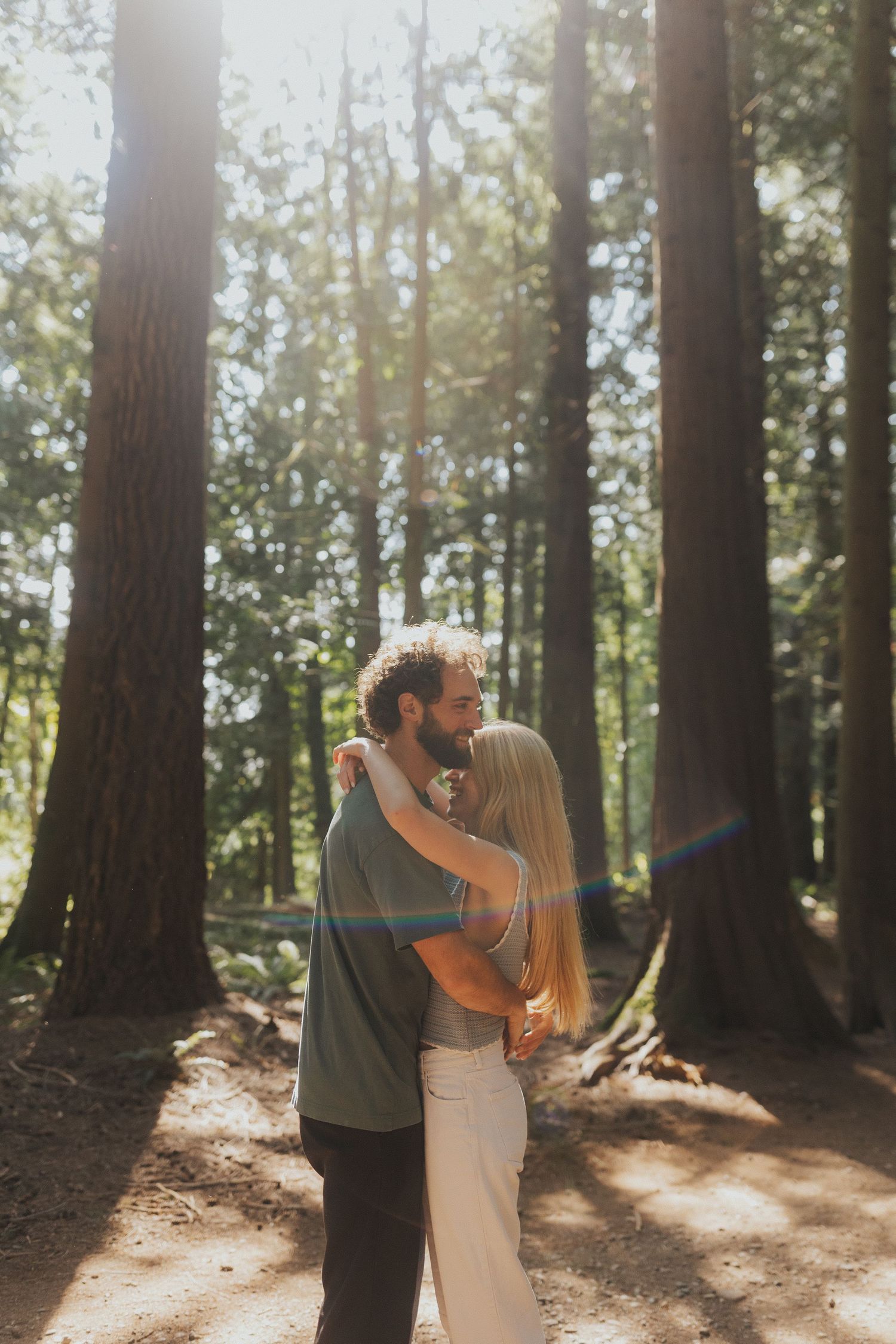 Sunlight streams through tall trees as a couple dances together in a serene forest setting.