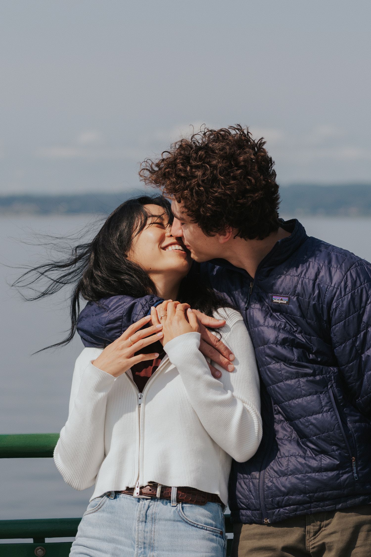 A romantic moment unfolds between two people on a seaside viewing platform under blue skies.