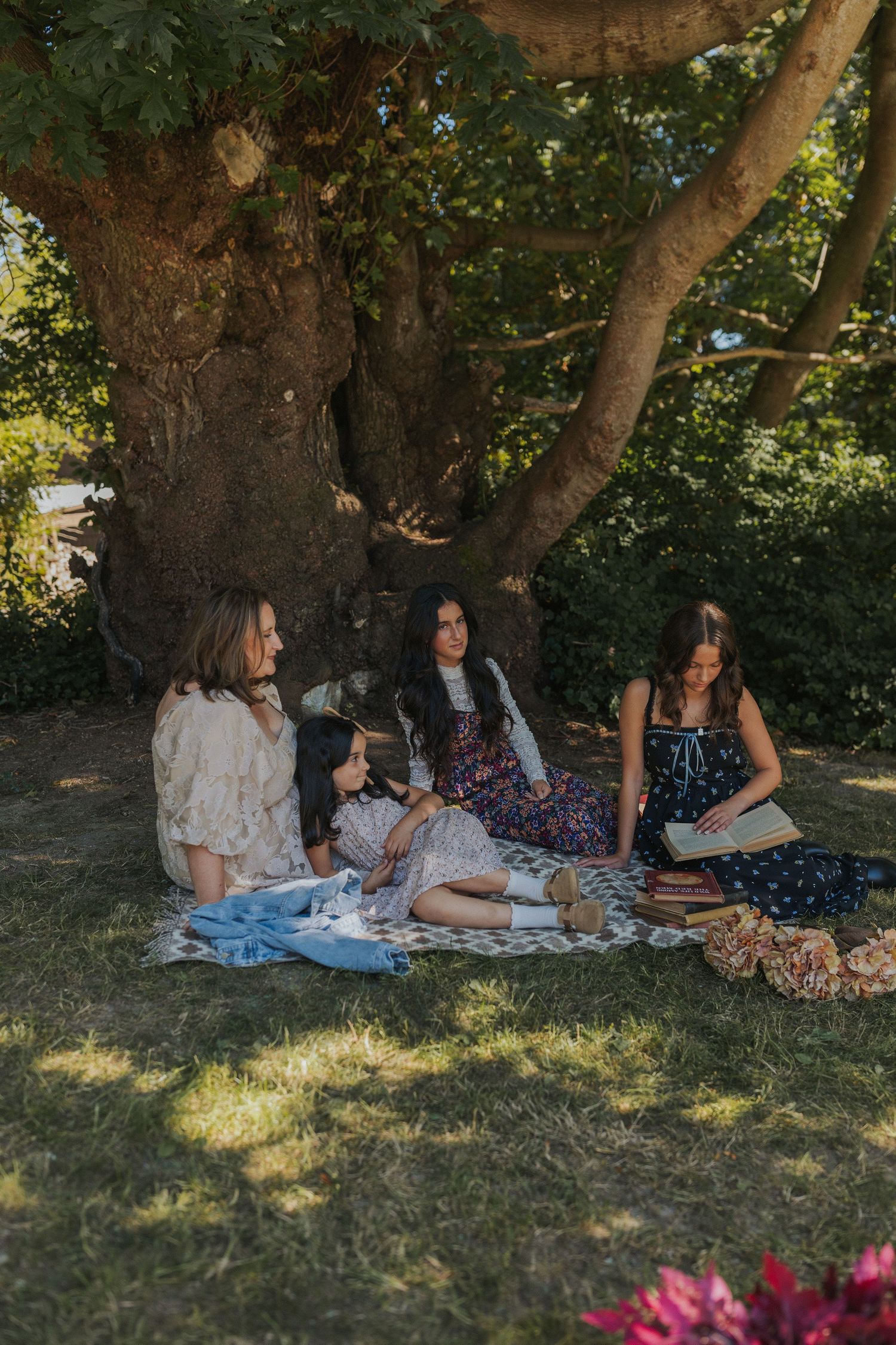 A picnic scene under a large tree with blankets spread on the grass.