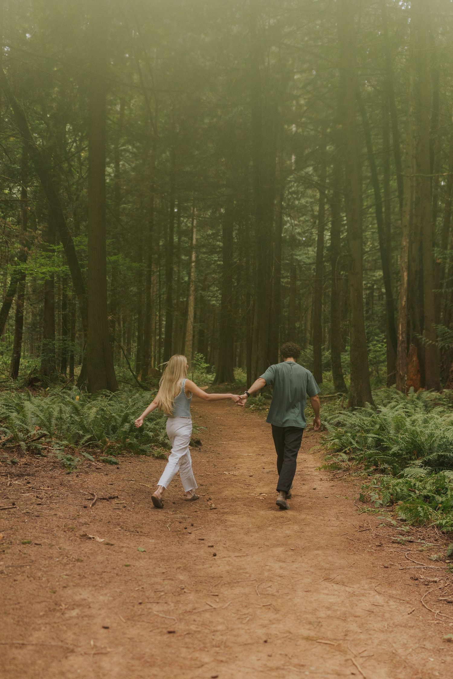 Couple walking together on a dirt path through a lush green forest.