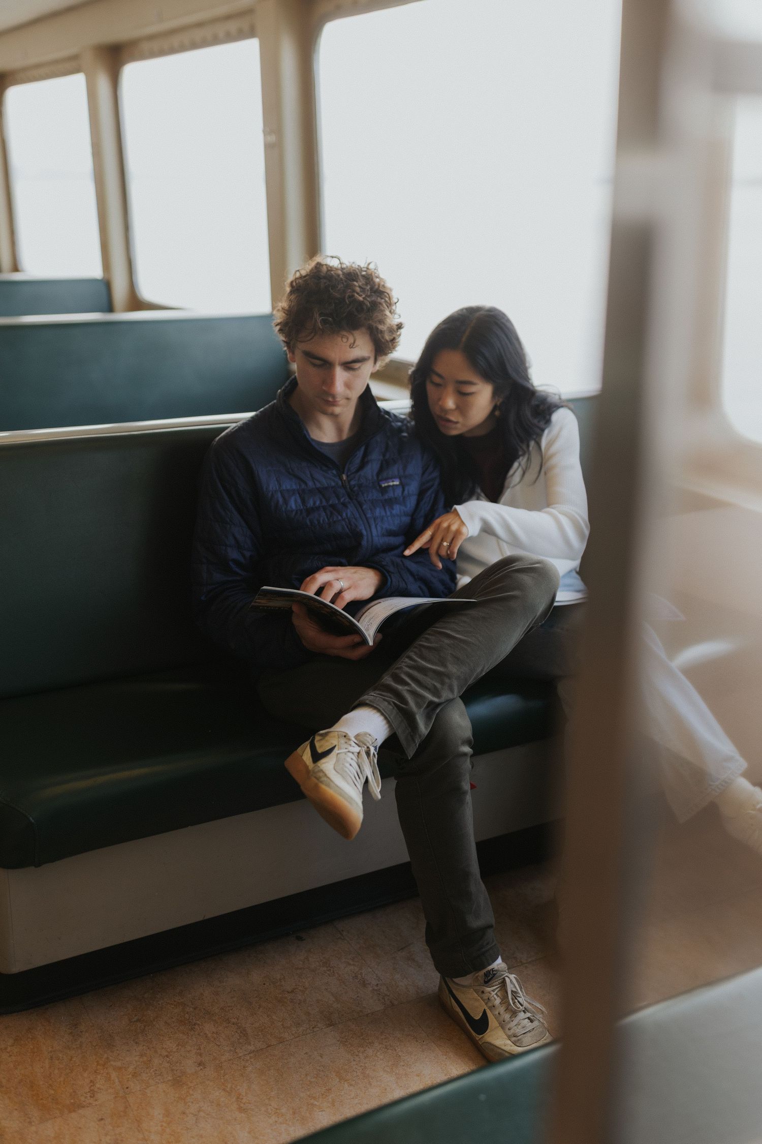 Two people sitting together on ferry bench, looking at device screen.