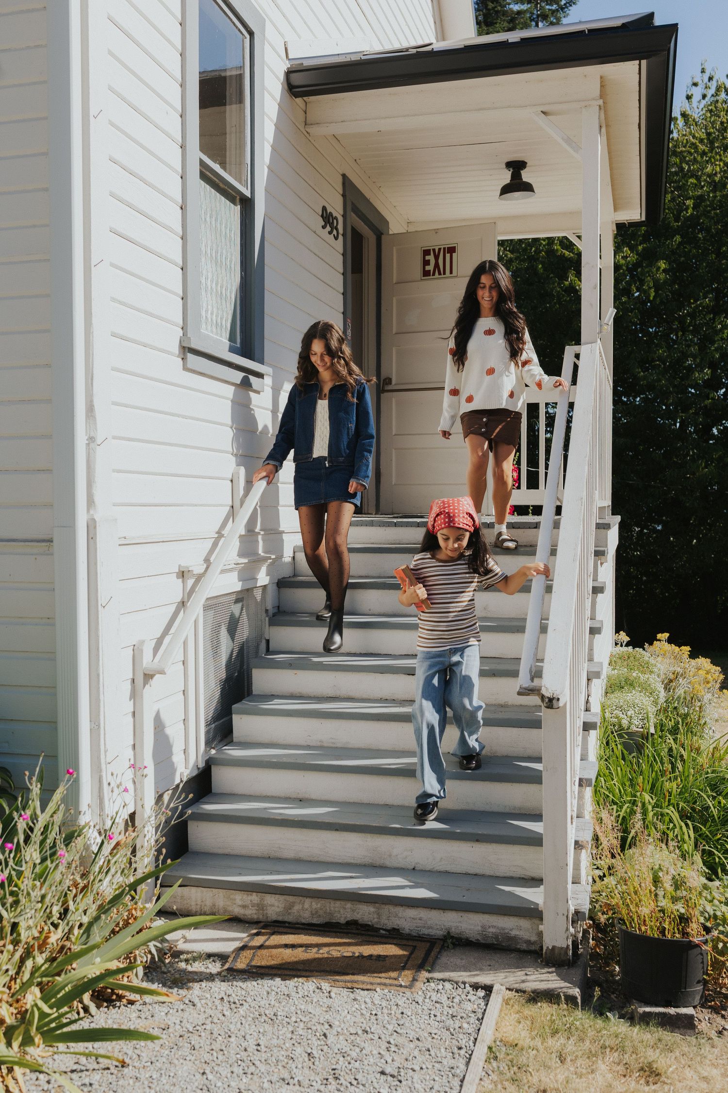 People walking down white painted wooden stairs of a house entrance with an exit sign.