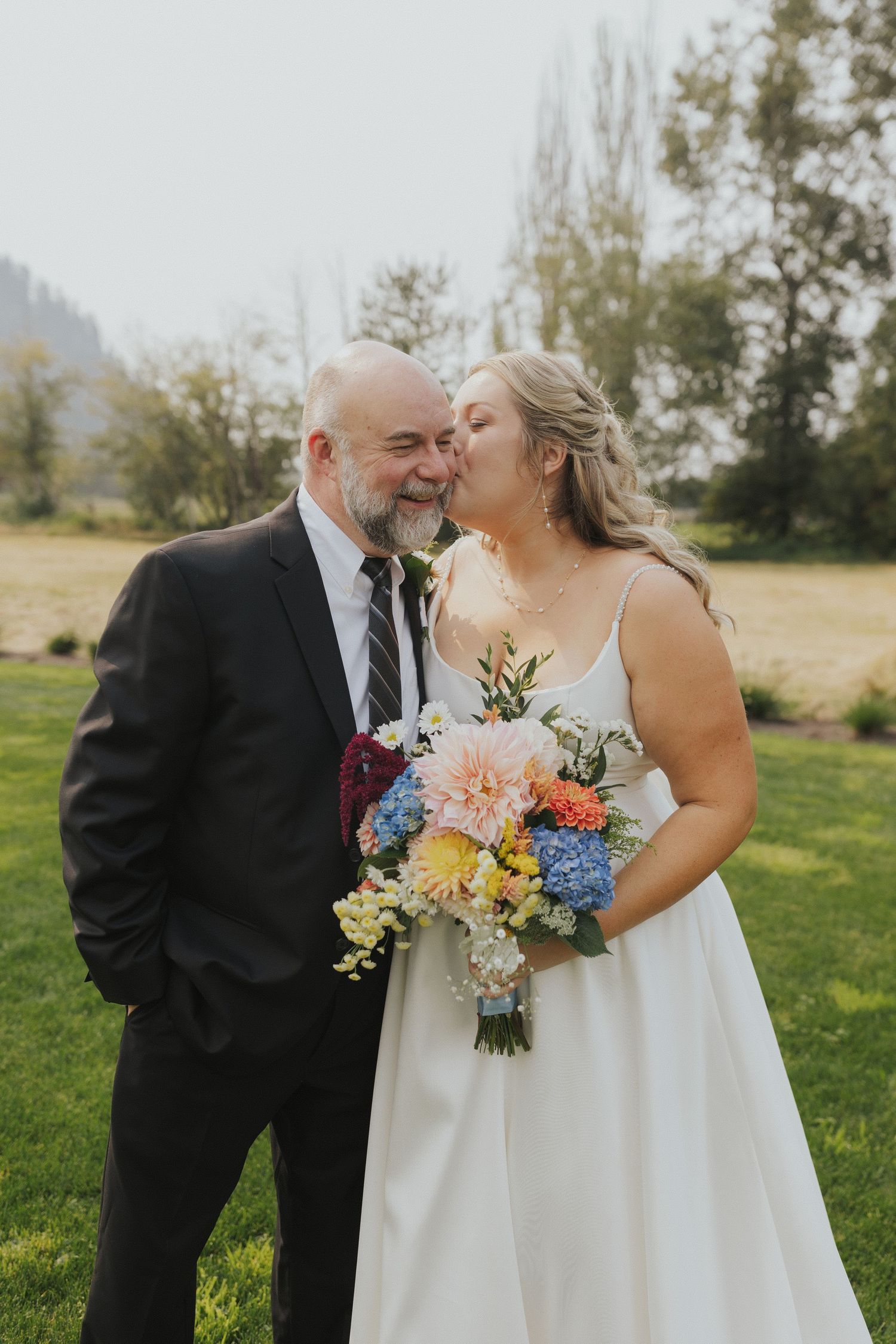 Wedding couple shares a romantic moment with vibrant wildflower bouquet in an outdoor setting.