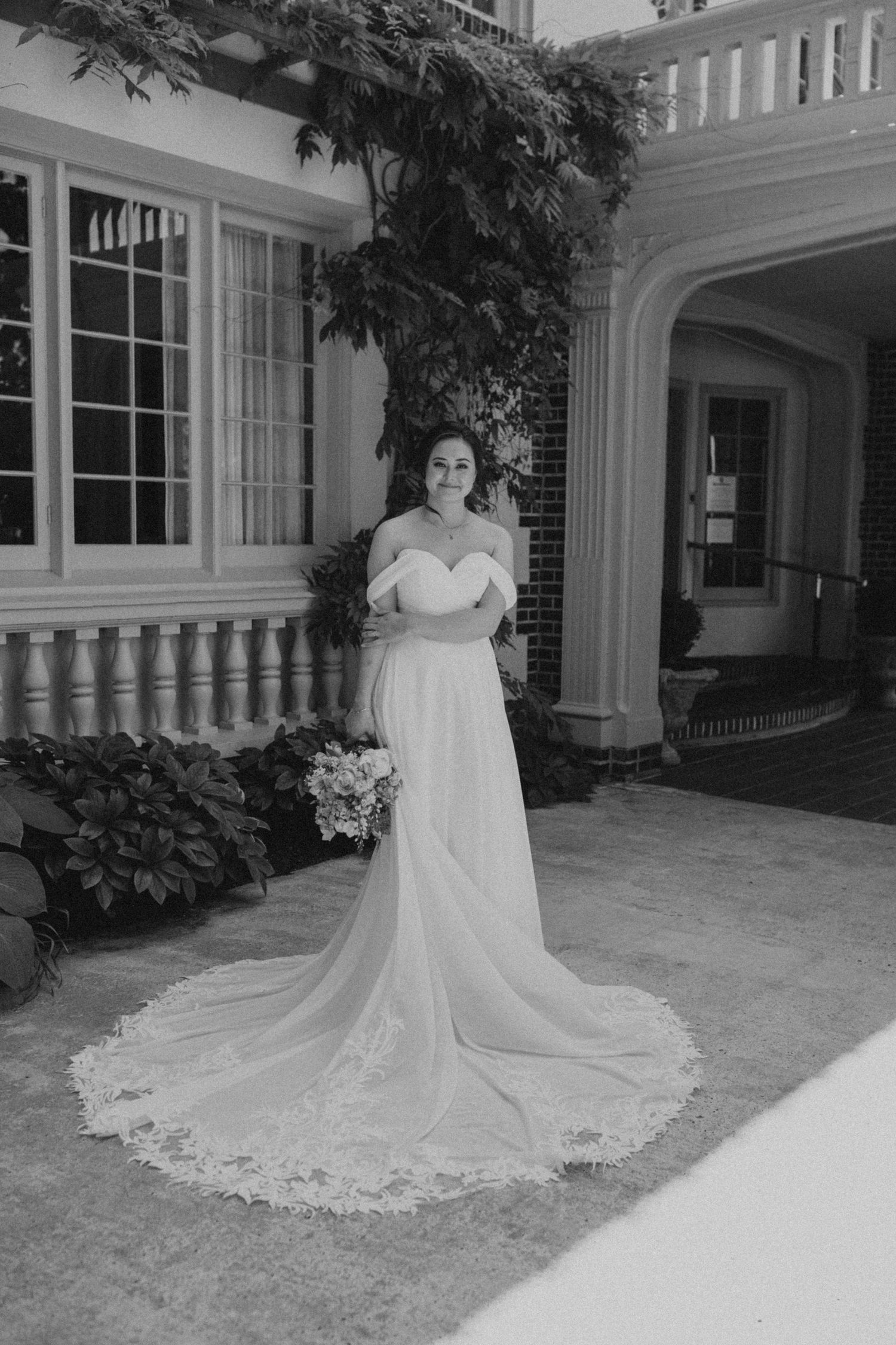 Elegant bridal gown with long lace train displayed against cream colored building exterior.