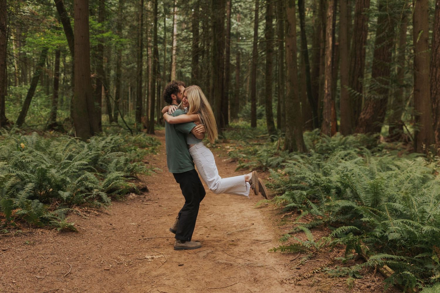 Romantic forest photoshoot with couple walking among ferns and trees.