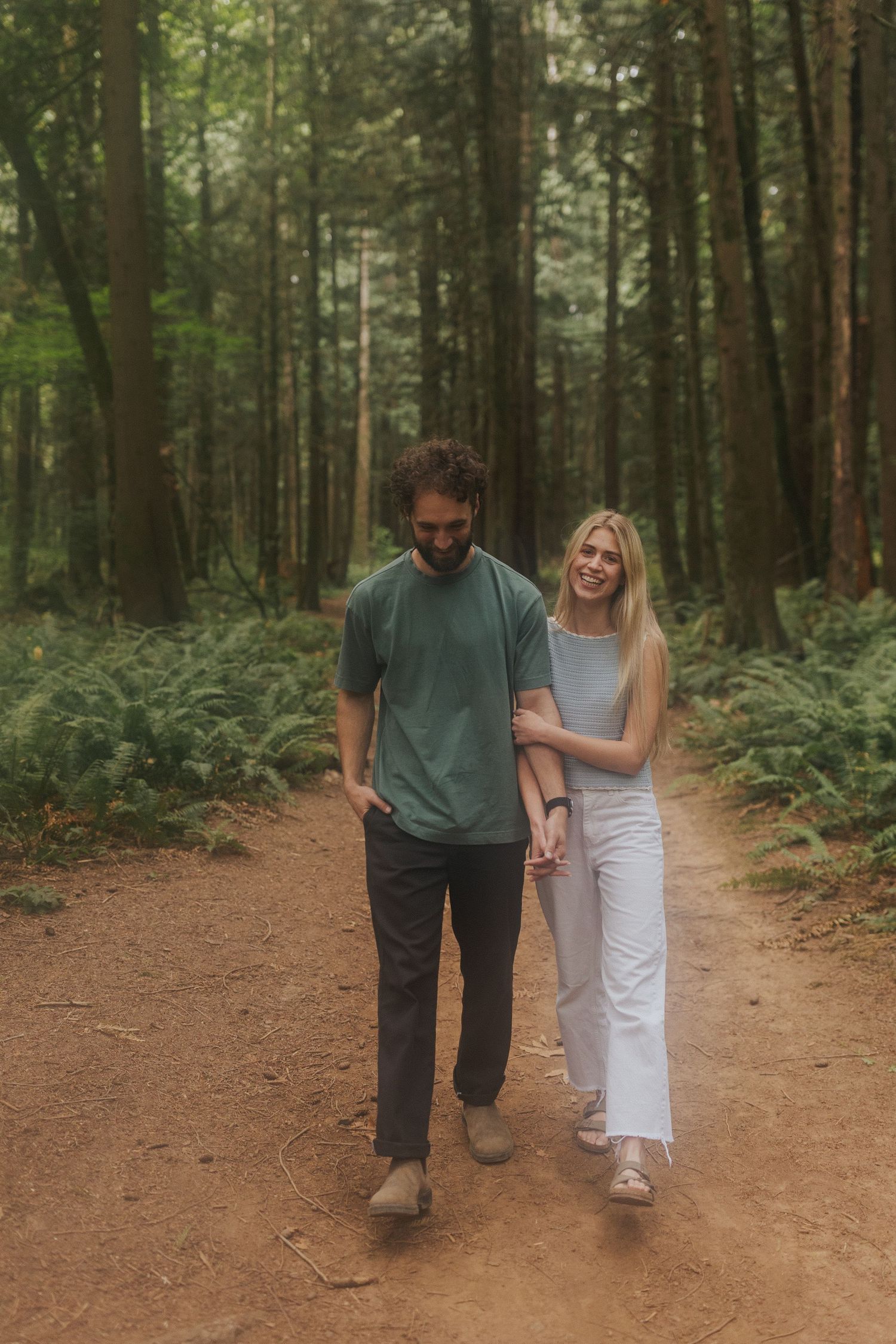 Couple walking hand in hand down a dirt trail through a Pacific Northwest forest.