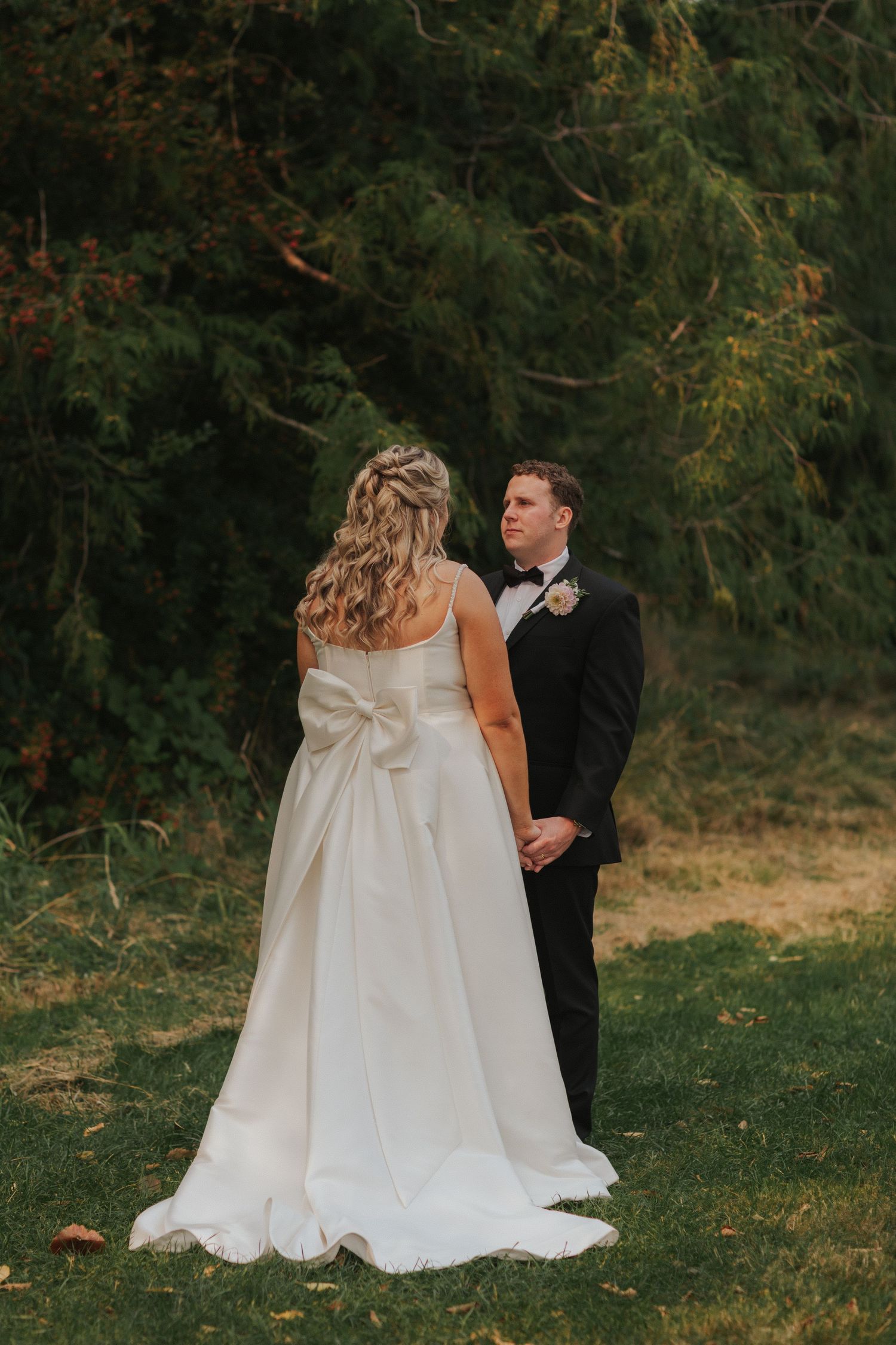A wedding couple in white dress and black suit embrace on a grassy slope during their photo session.