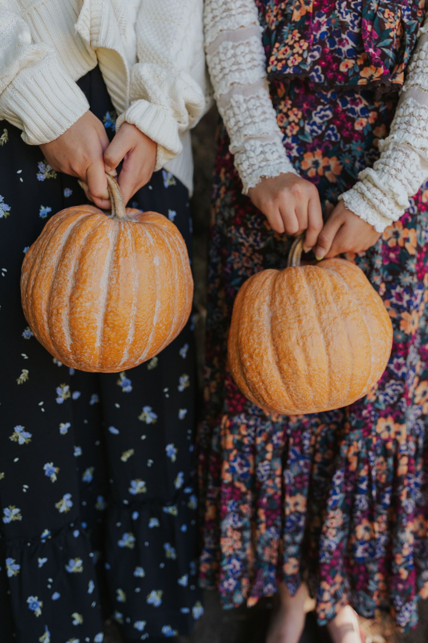 Hands in white sweater sleeves carve designs into an orange pumpkin.