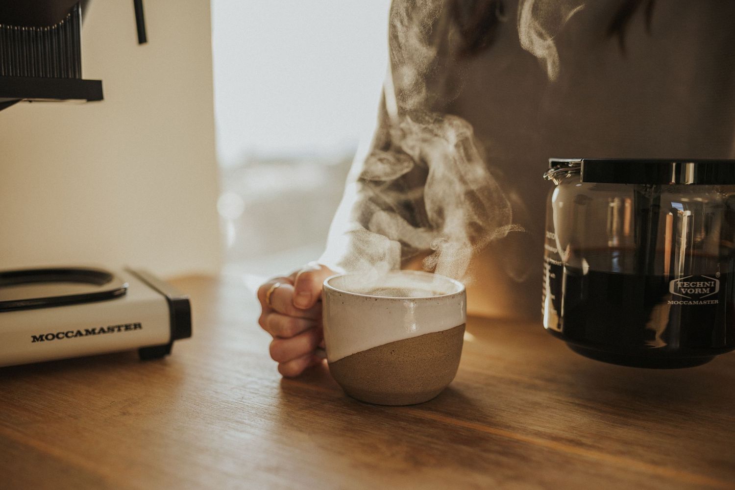 Coffee maker and brewing equipment on wooden counter in warm ambient lighting.