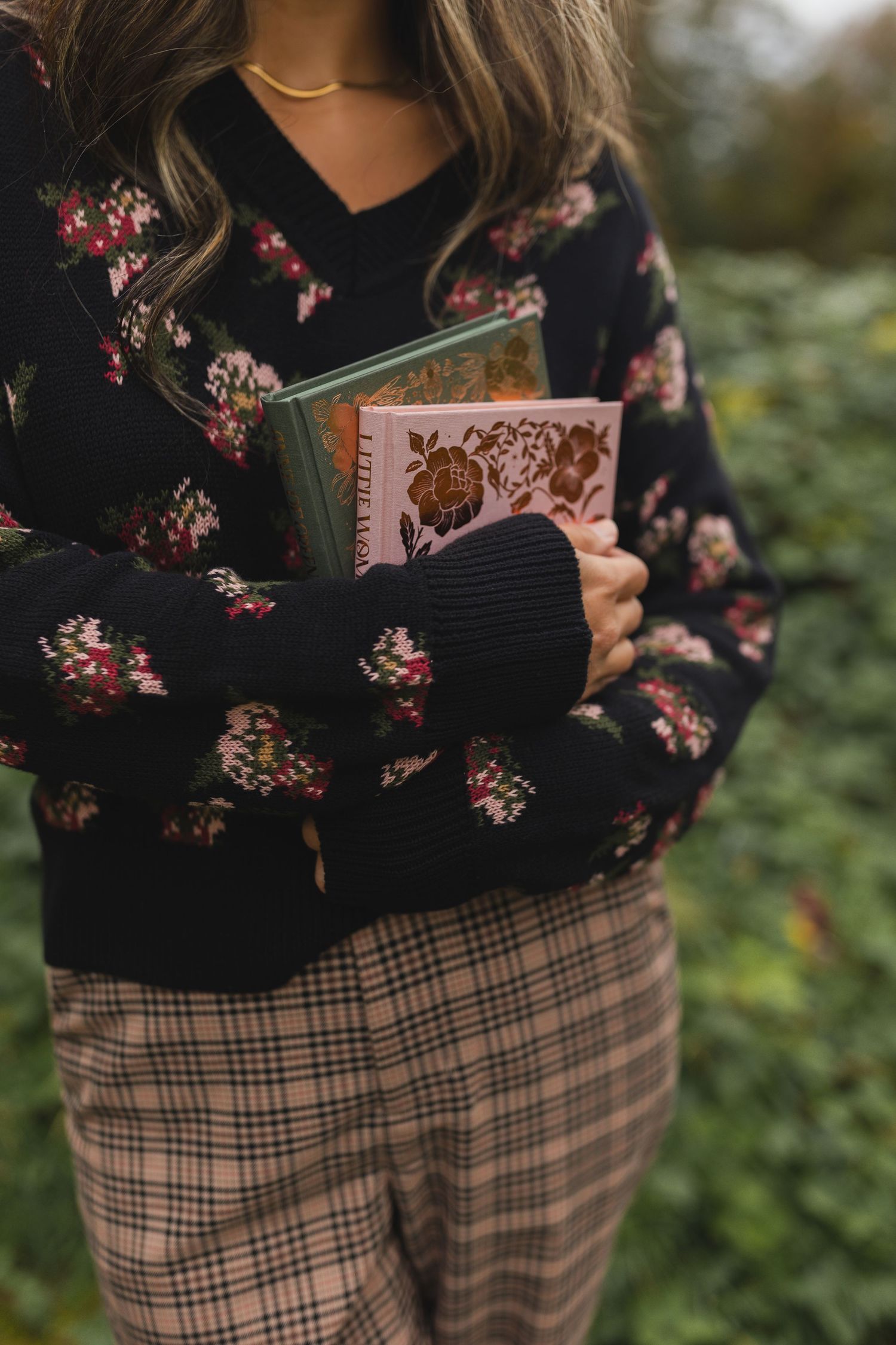 Close-up shots of a floral black sweater paired with plaid pants holding vintage books.