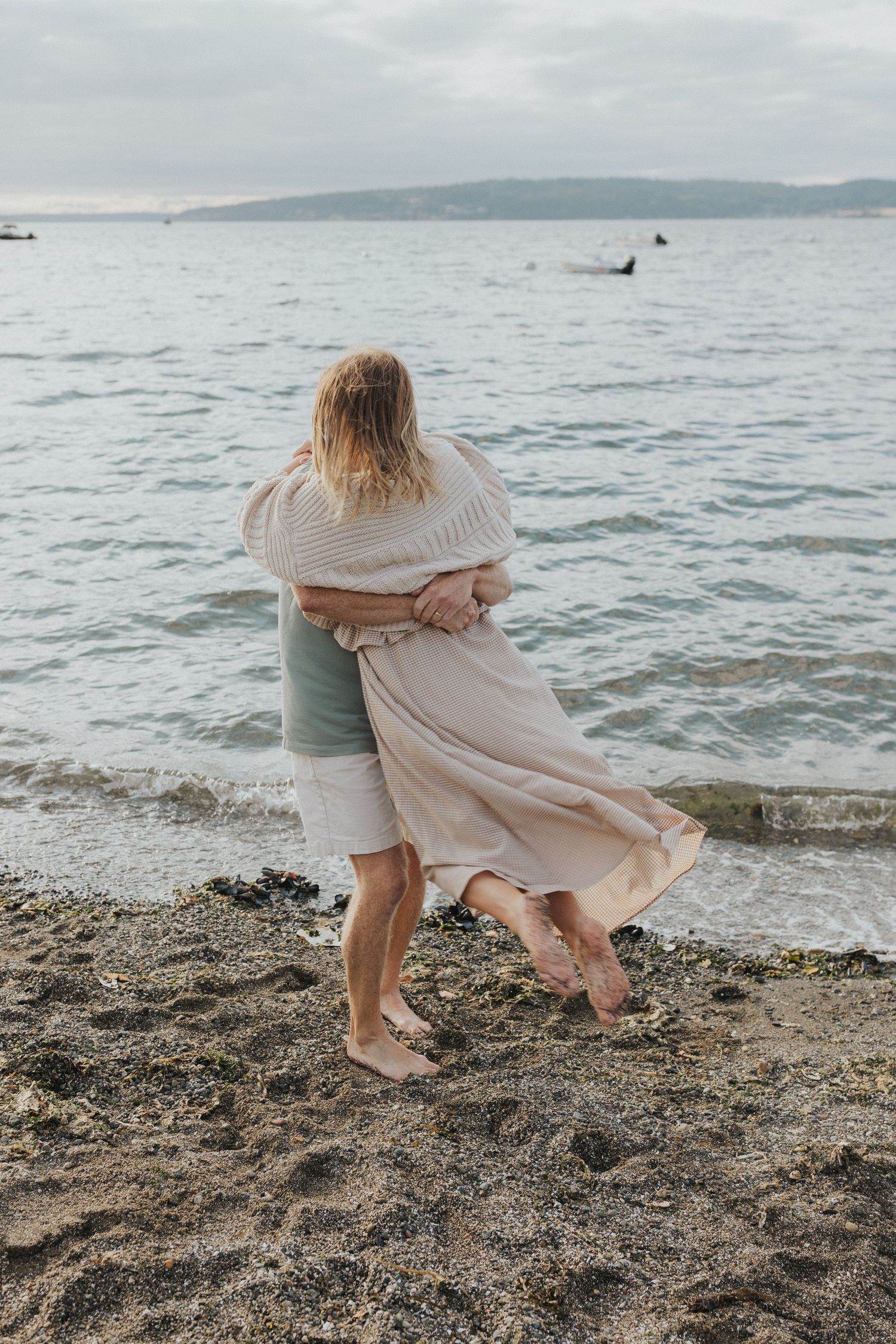 Tender embrace captured on a pebble beach with ocean waves in background.